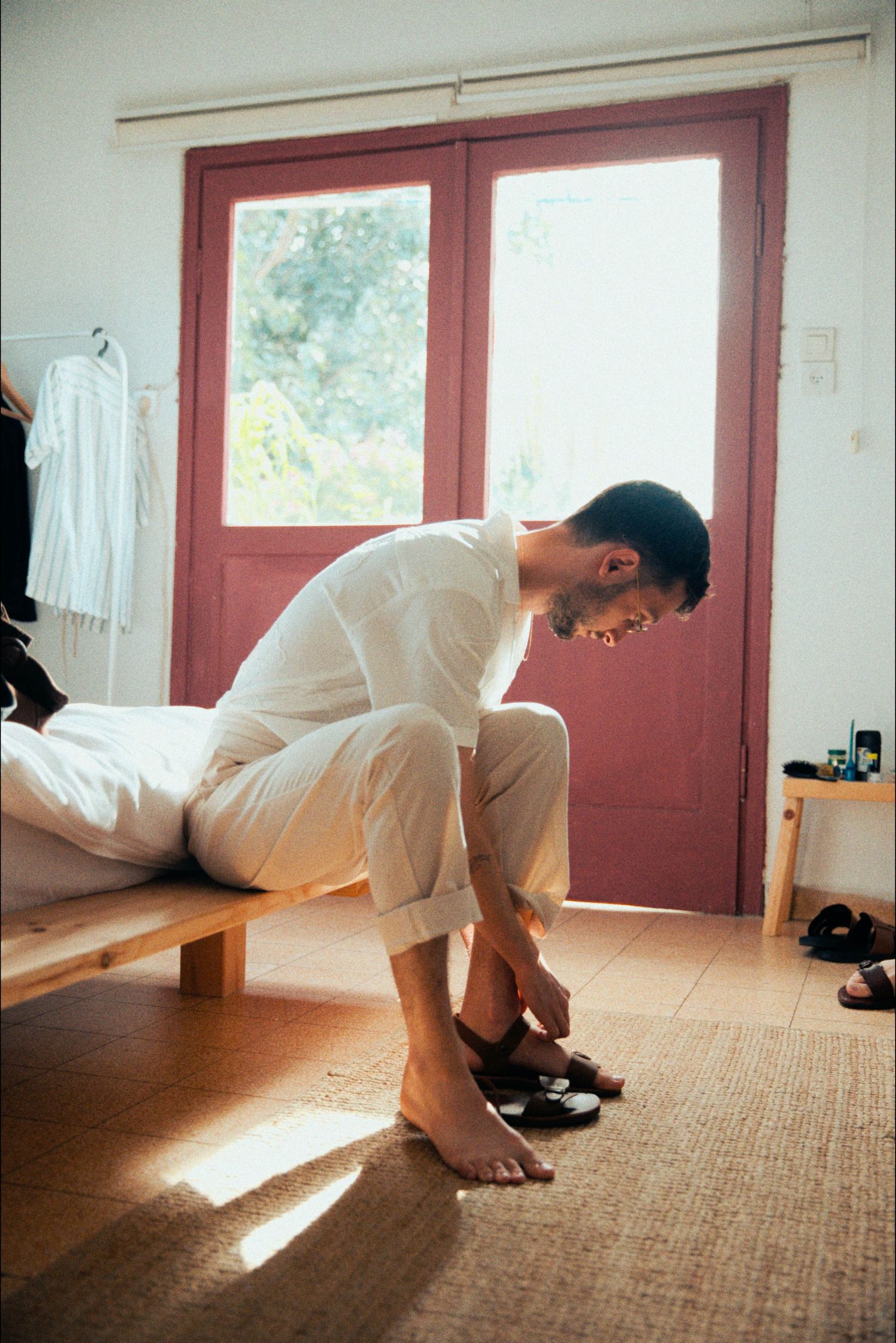 Person in white clothing stretching on a carpeted floor in a sunlit room.