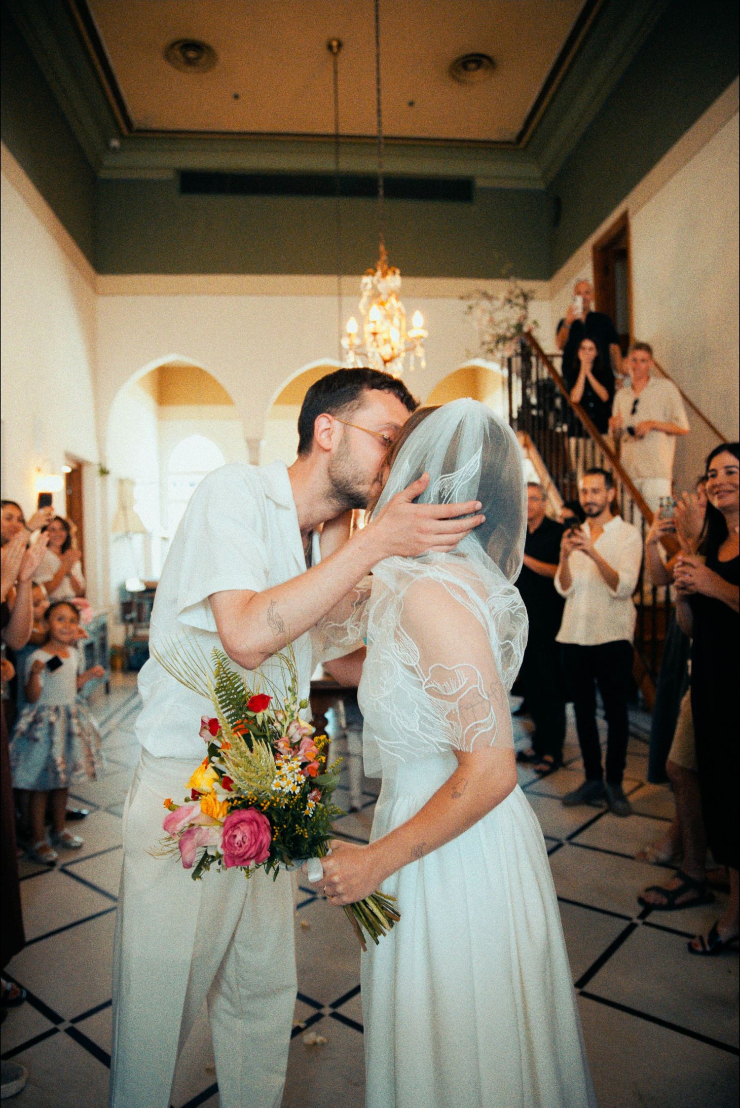 A romantic kiss between newlyweds while holding a colorful bouquet.