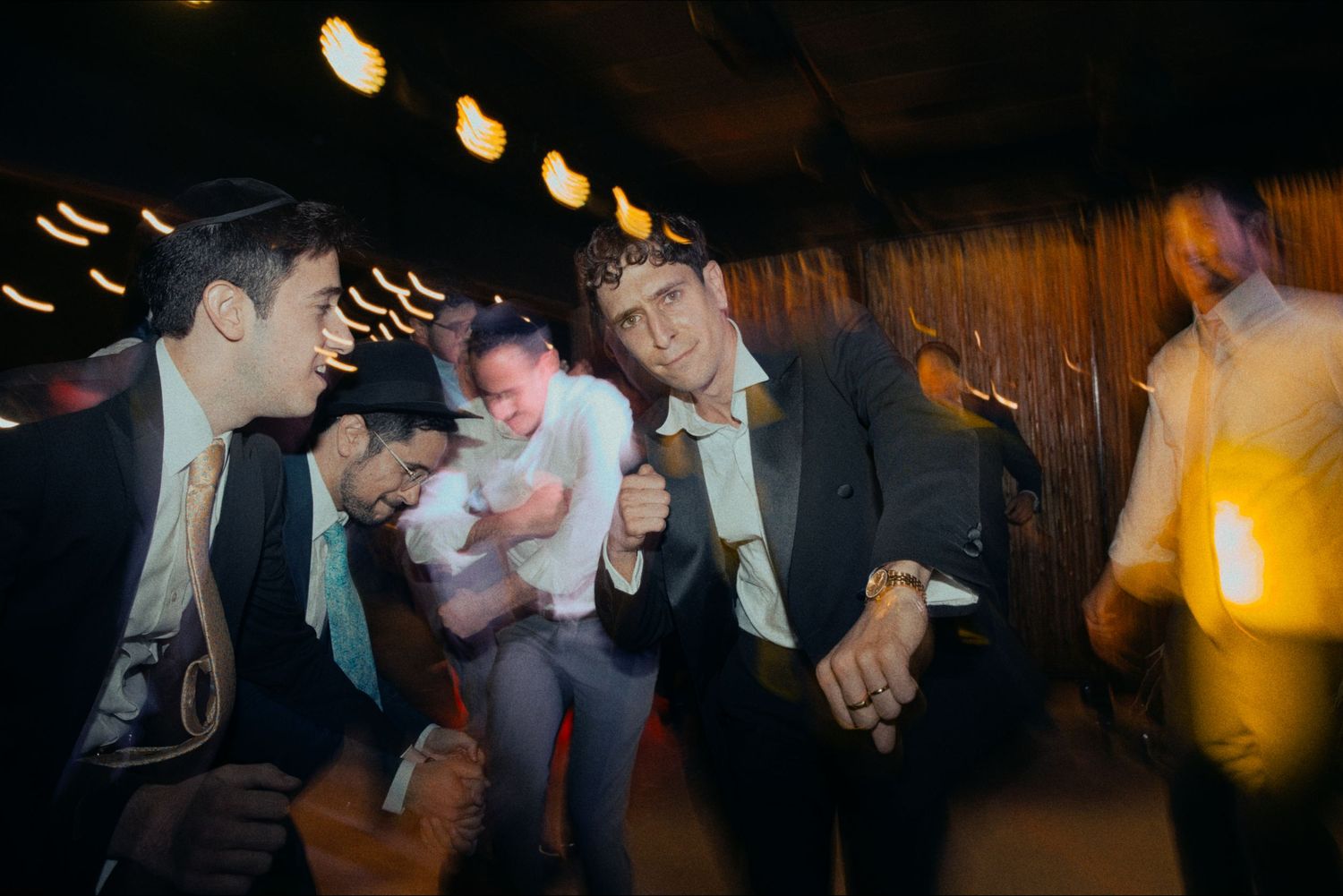 Friends in formal attire sharing laughs and dancing at a dimly lit indoor celebration.