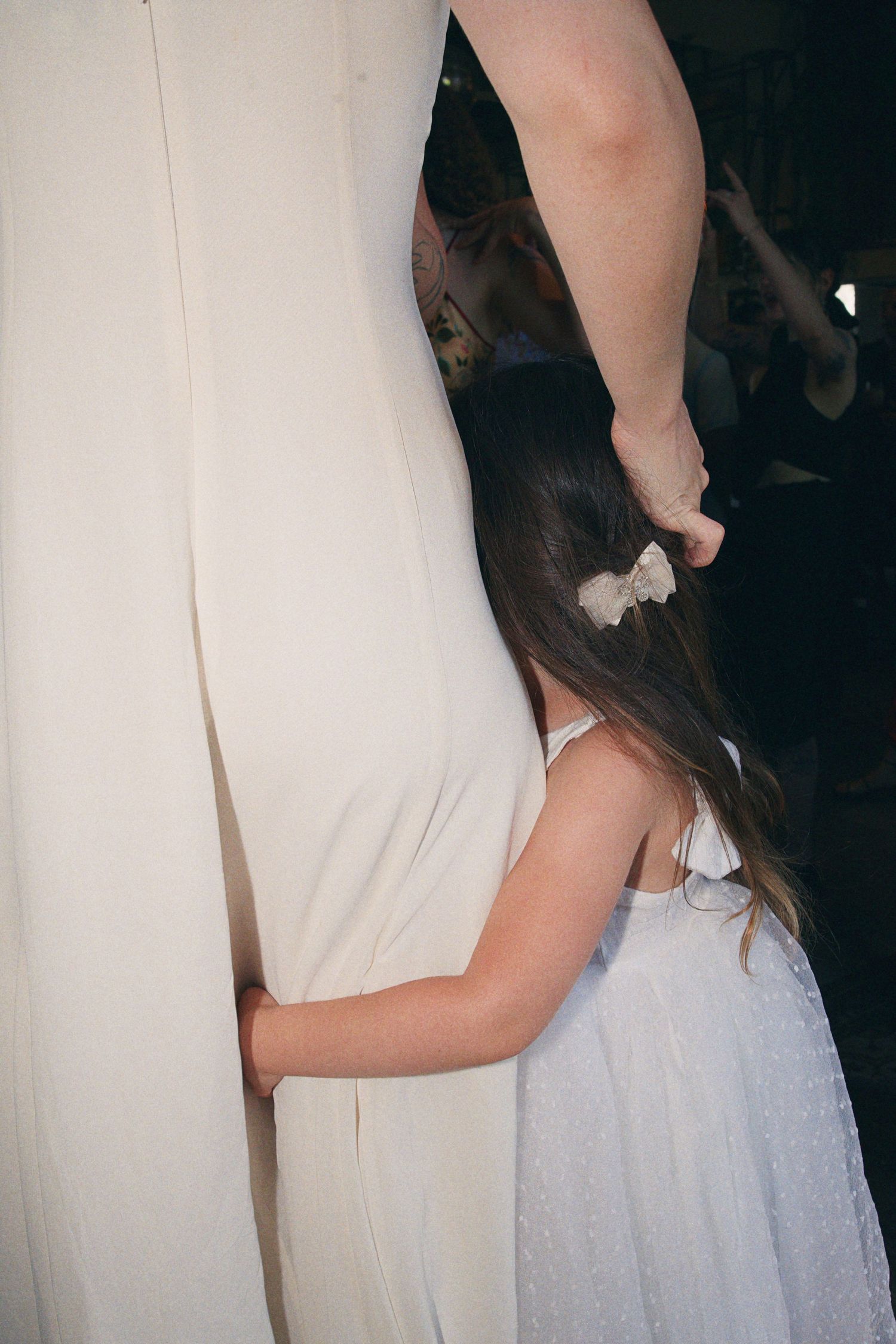 Young flower girl in white dress holding bride's gown during wedding ceremony.