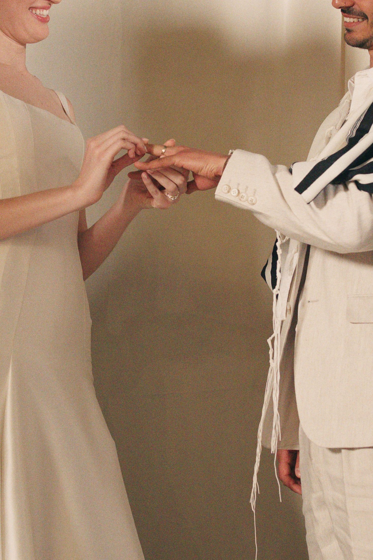 Bride in ivory gown places wedding ring on grooms finger during elegant ceremony exchange.