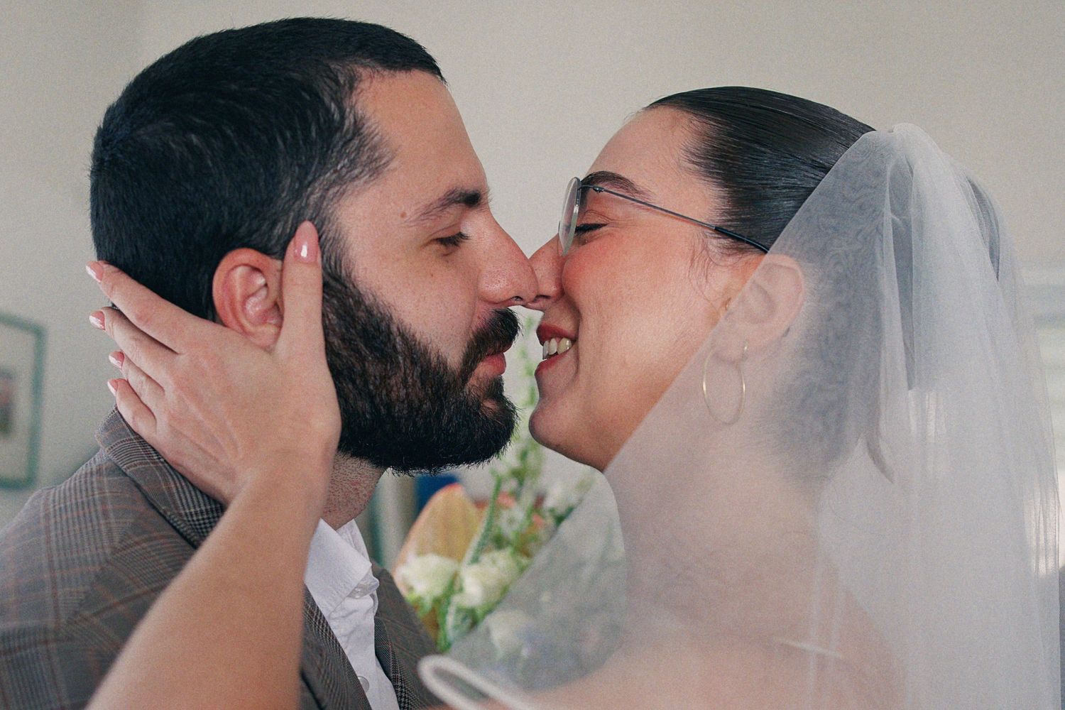 A bride and groom share a romantic almost-kiss moment, with the bride wearing a veil and holding a bouquet.