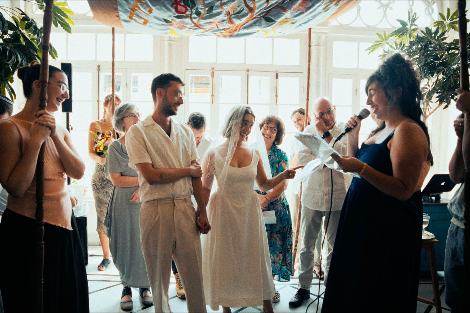 People dancing and celebrating in a bright sunlit room with decorative banners overhead.