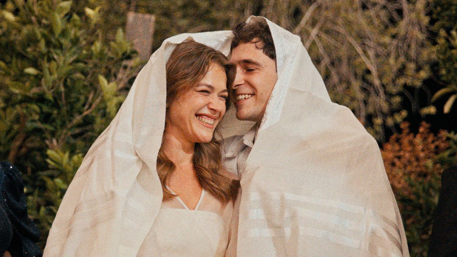 Intimate moment shared under white wedding veil during outdoor ceremony.