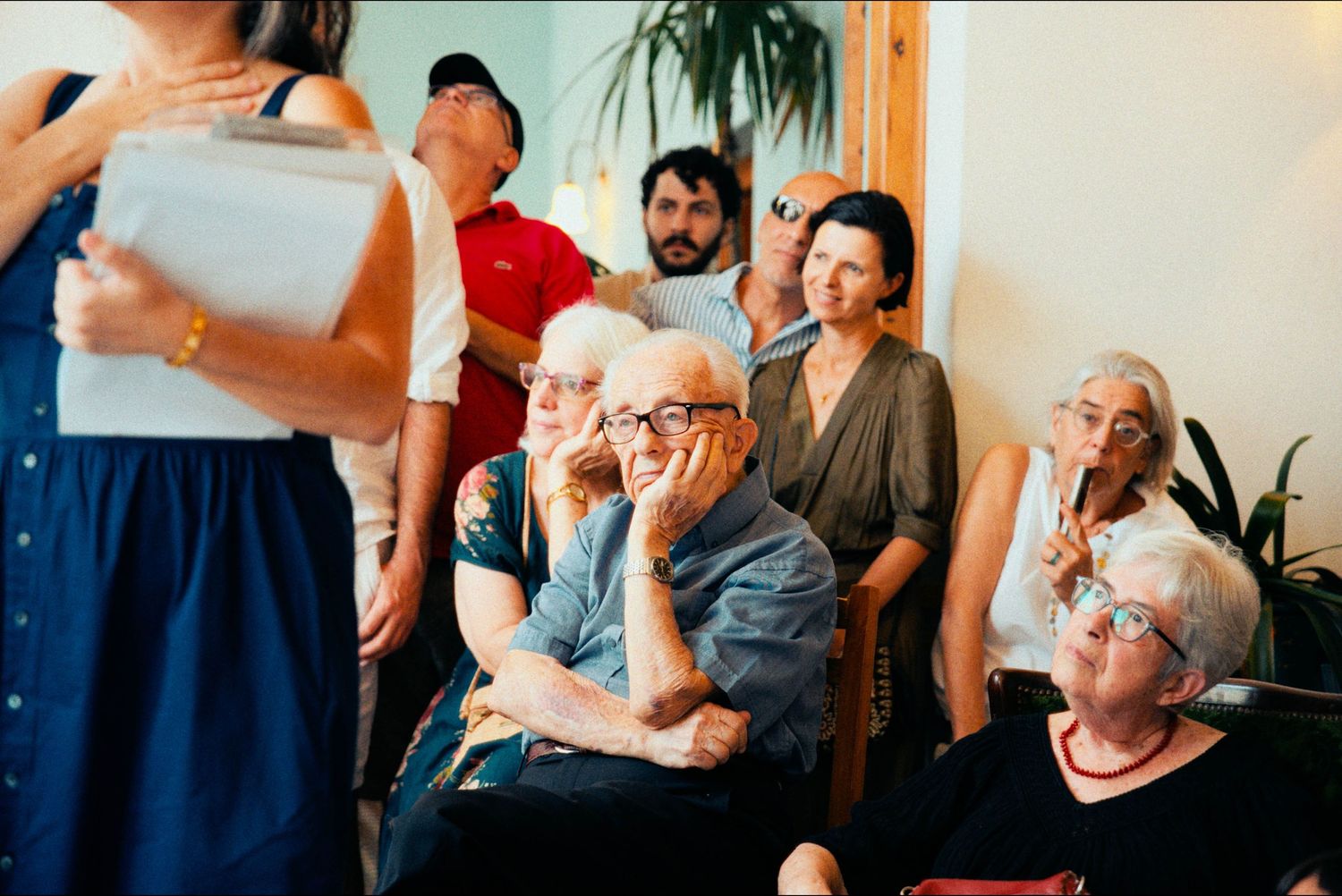 Wedding guests watch attentively during an indoor ceremony with houseplants in the background.