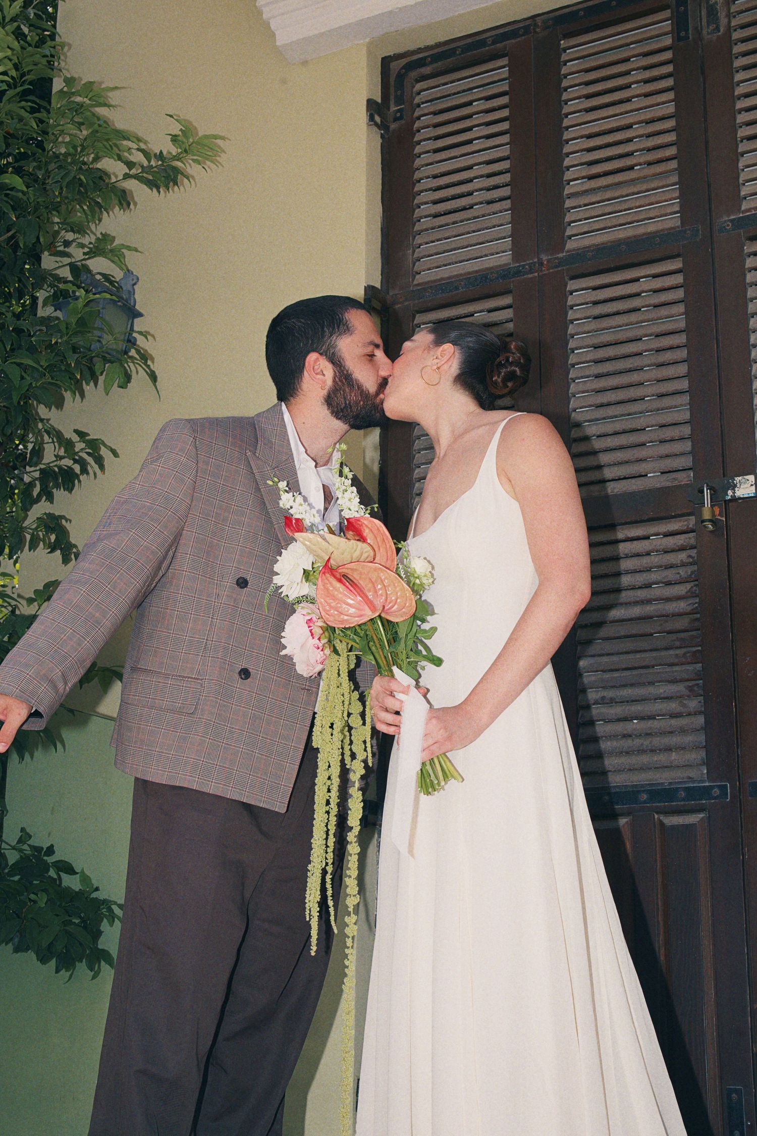 Bride and groom sharing a kiss outdoors, bride holding a tropical pink and green wedding bouquet.