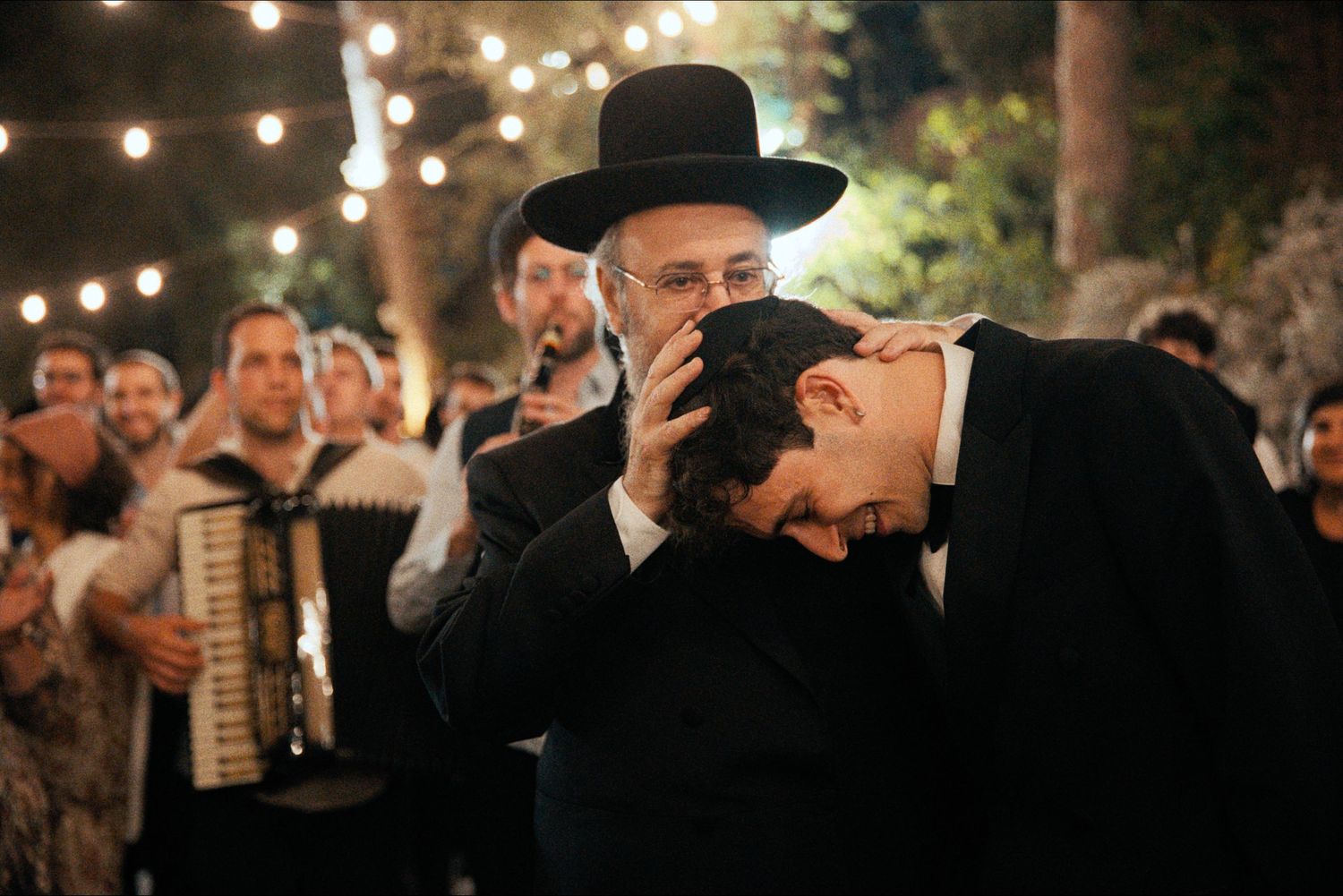 Guests in formal attire gather under twinkling lights at an outdoor evening celebration.