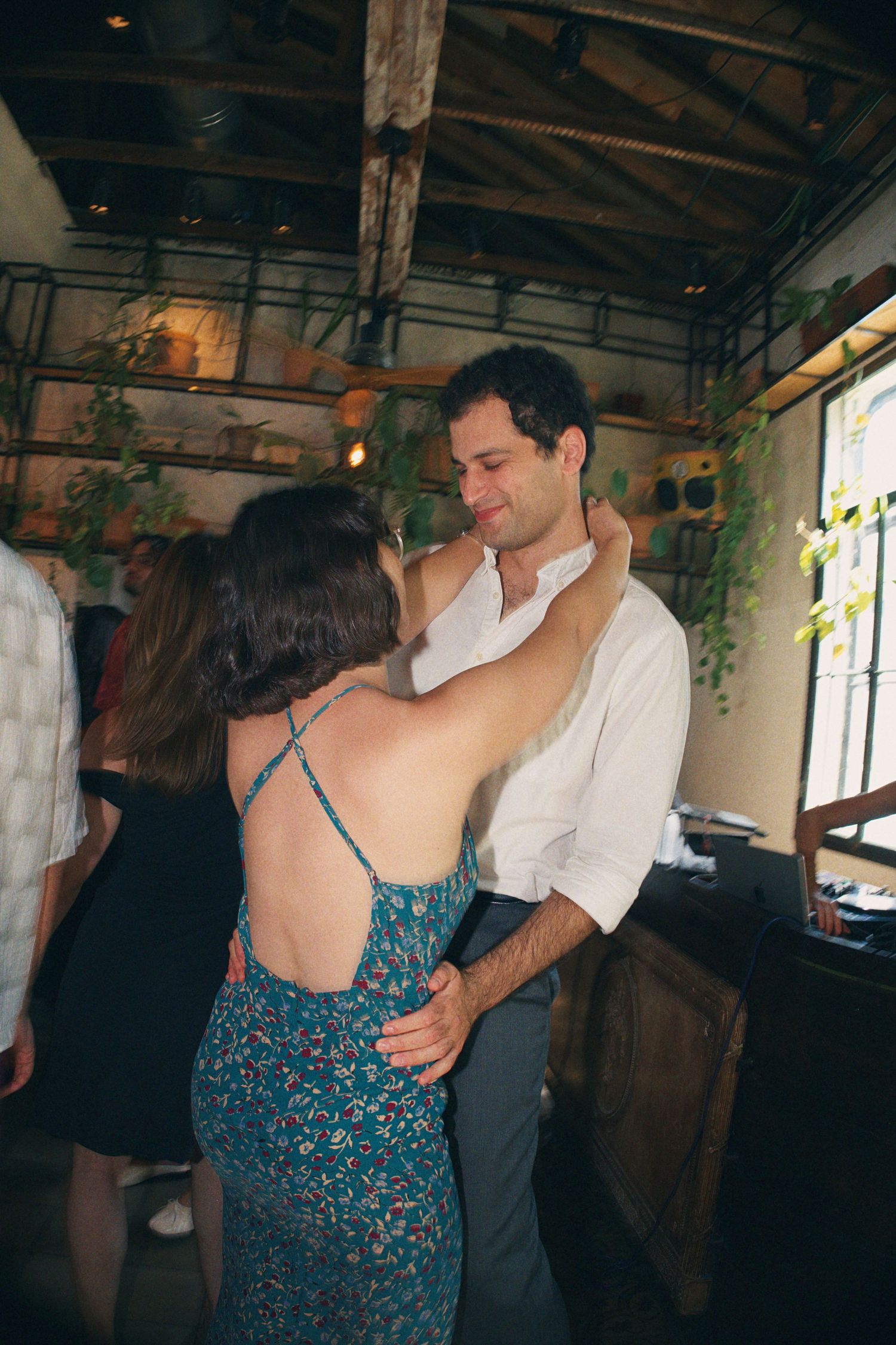 Couple dancing together in a rustic indoor venue with hanging plants and exposed wooden beams.