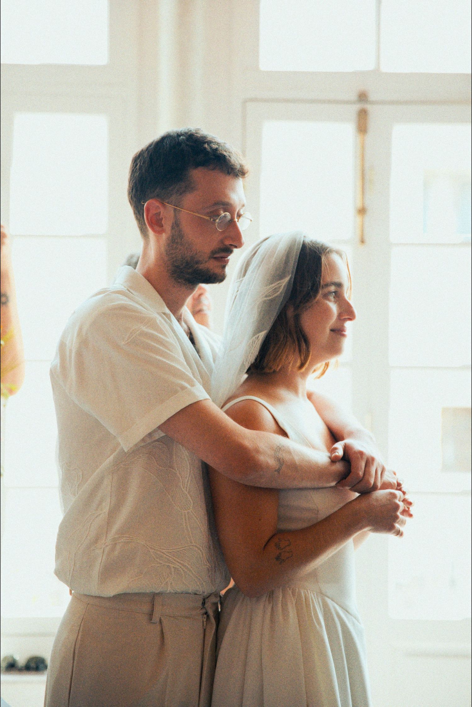 Couple in white attire dancing together in a sunlit room.