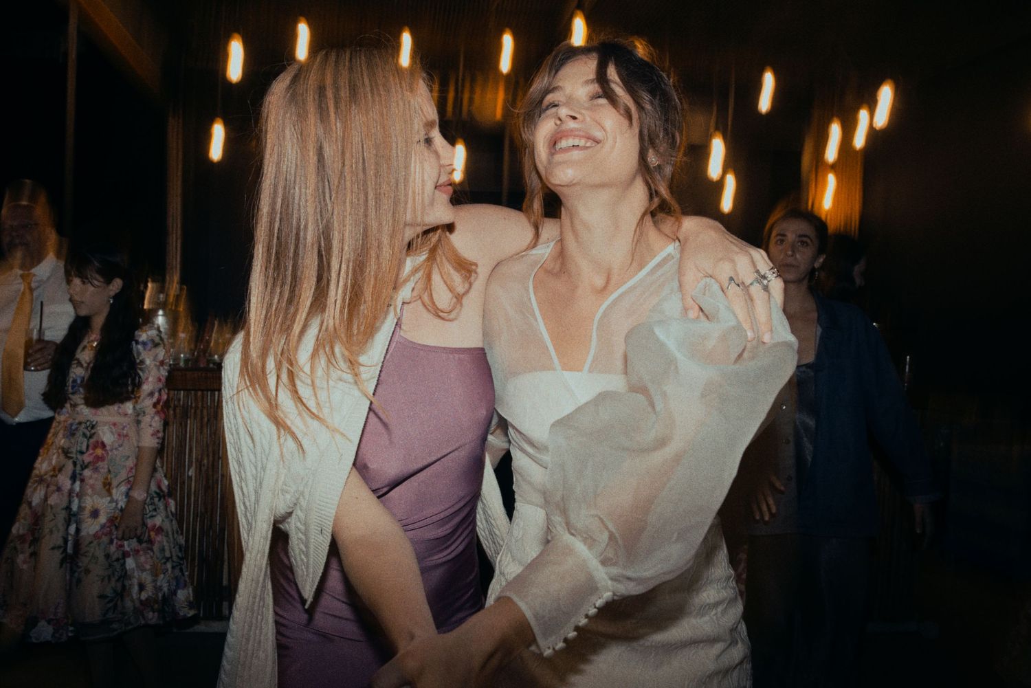 Two party guests share a joyful moment dancing under warm lighting at an indoor celebration.