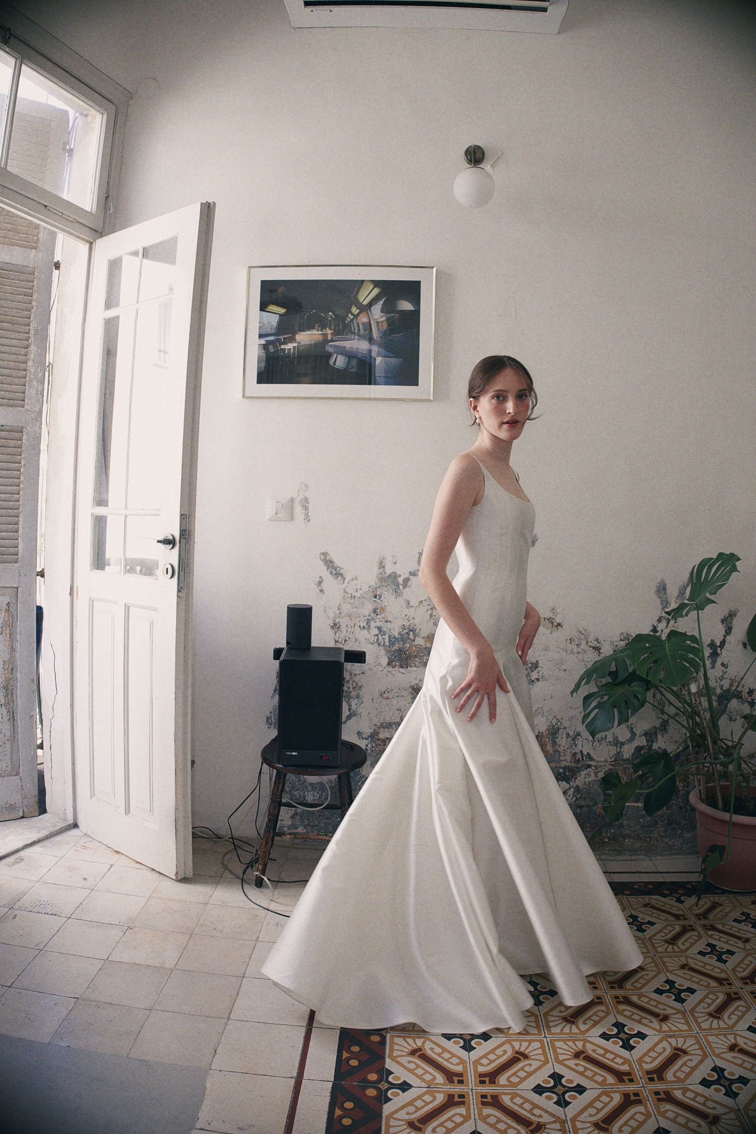 Bride in elegant white satin mermaid wedding dress posing in vintage room with ornate tiled floor.