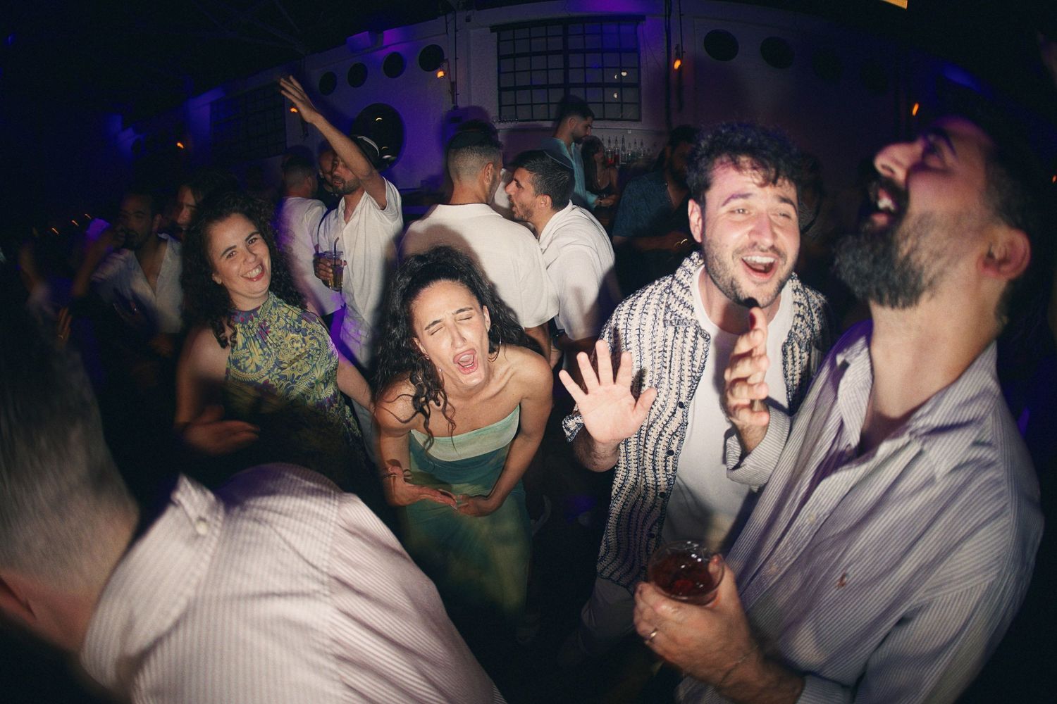 Guests laughing and dancing energetically on the dance floor at a festive wedding reception.