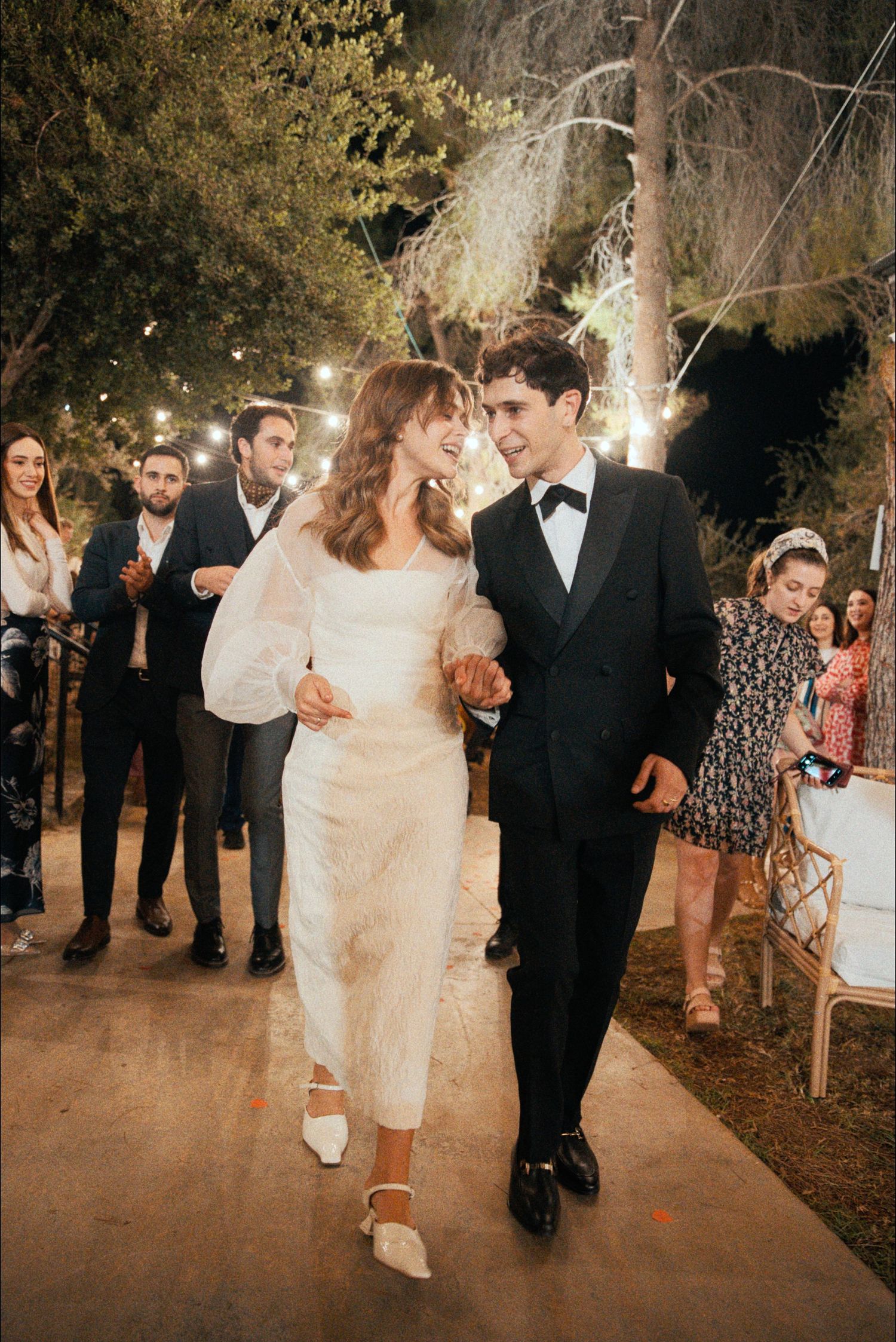 Wedding party walks along an illuminated outdoor path during evening celebration.
