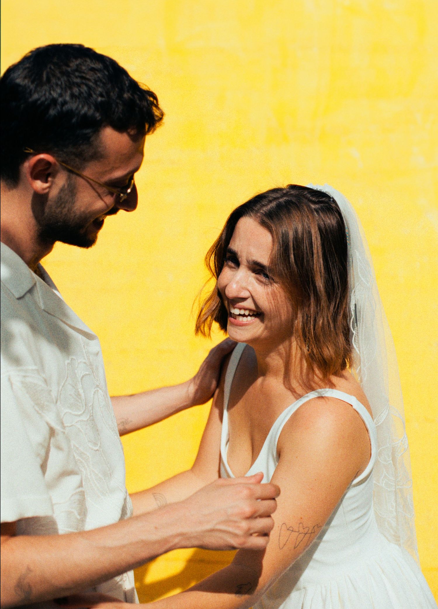 Candid wedding moments captured against a bright yellow wall in natural sunlight.