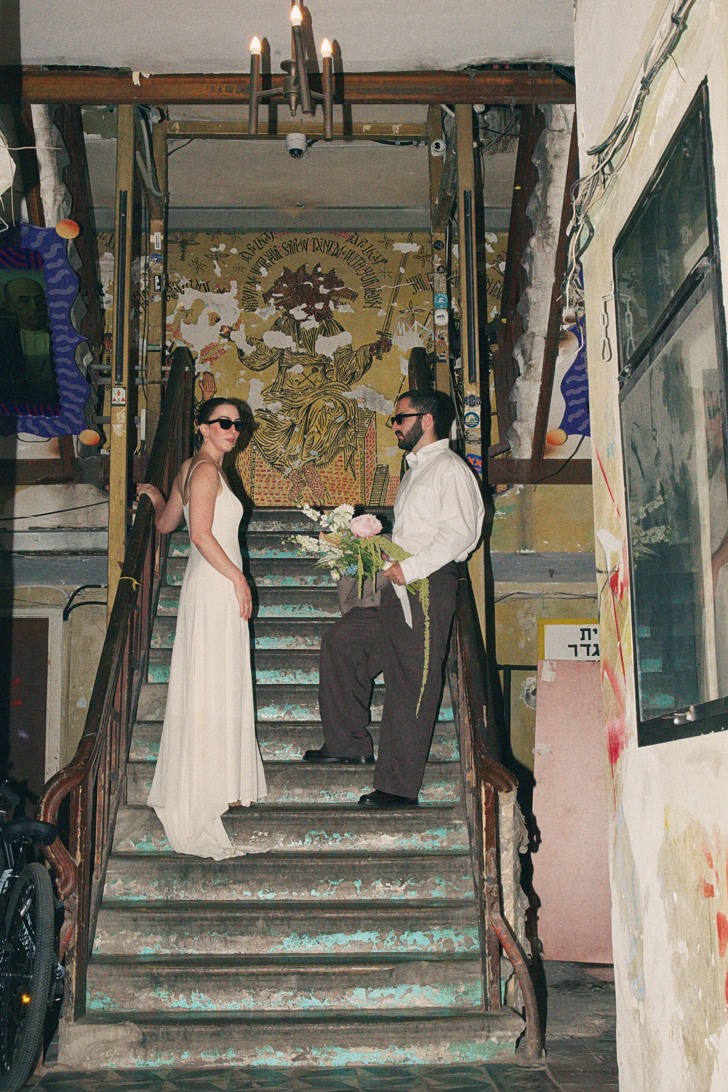Bride and groom stand on rustic staircase with bouquet in vintage venue.