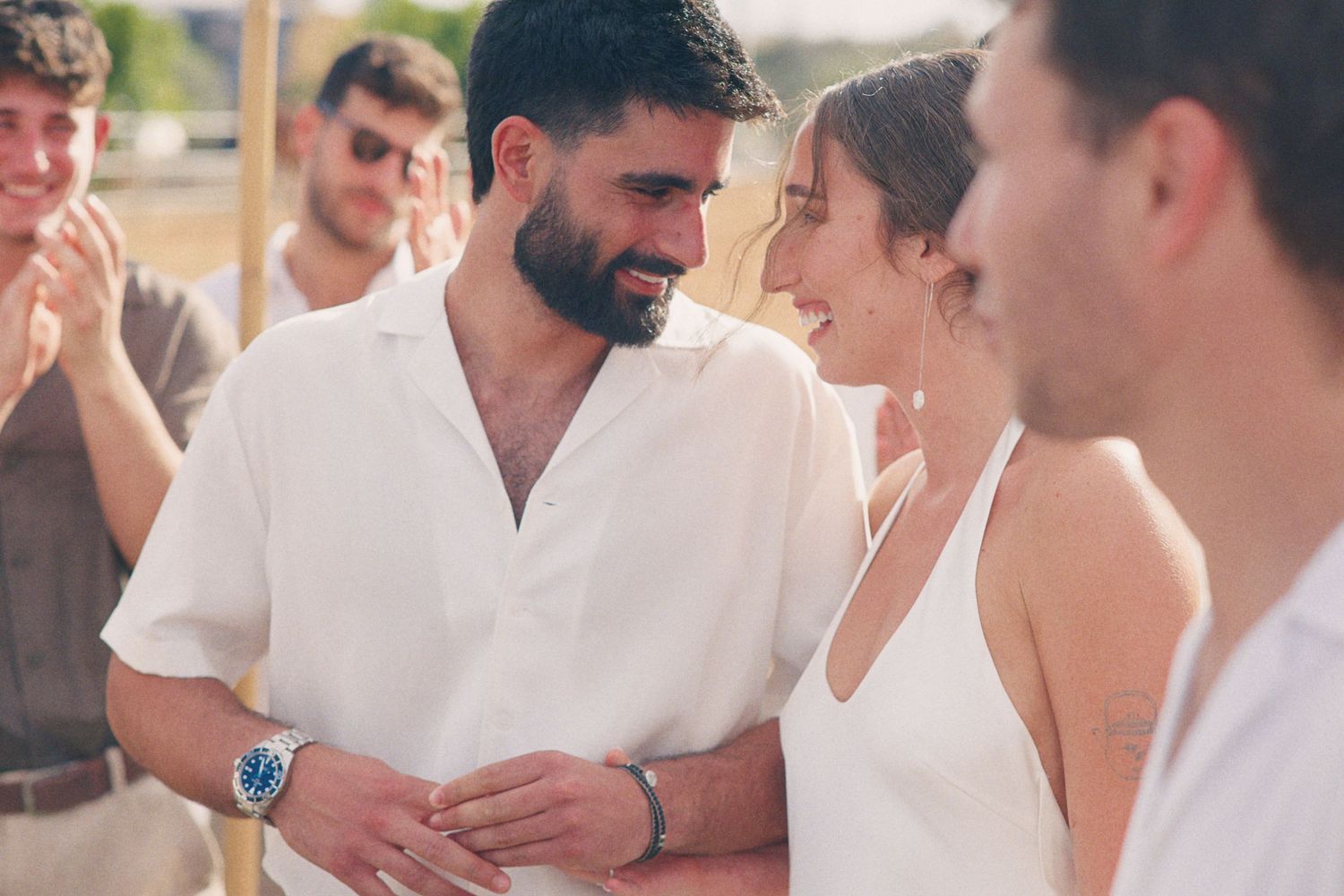 Bearded groom in white shirt shares a tender moment with bride in spaghetti strap dress at outdoor wedding.