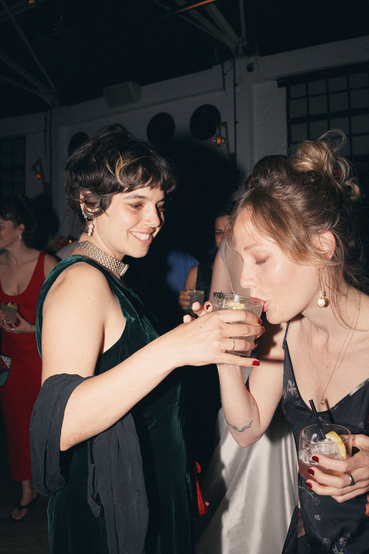 Two women in elegant dresses sharing a drink at a lively evening party event.