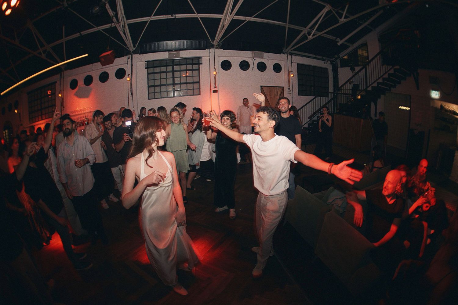 Two dancers perform energetically on a dance floor surrounded by a crowd in a dimly lit industrial venue.