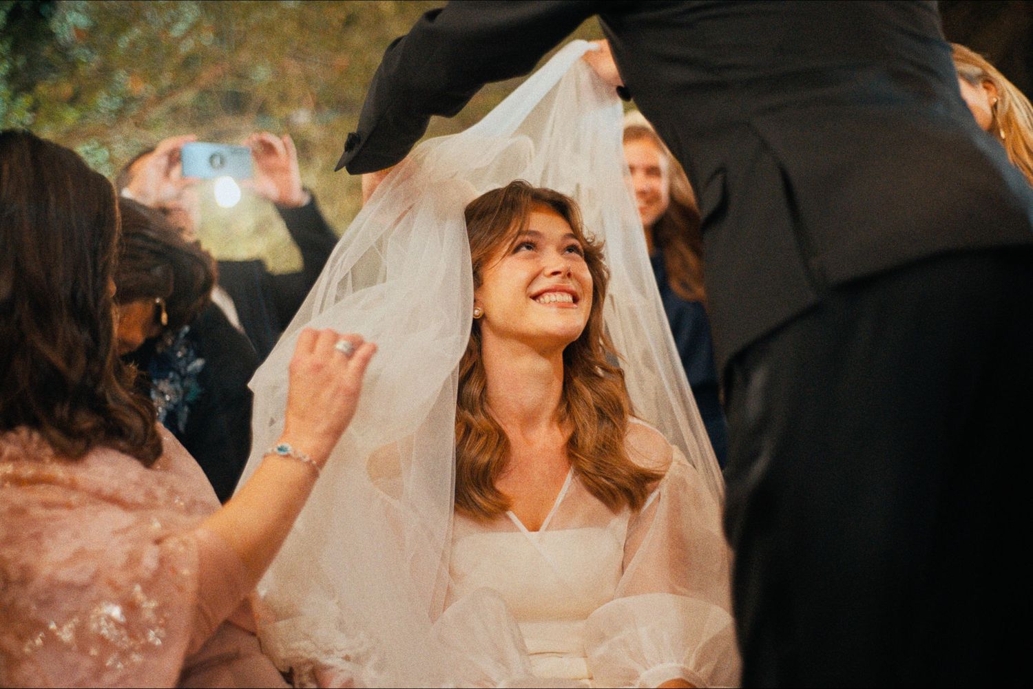A bride in a flowing white veil smiles during a joyful wedding celebration.