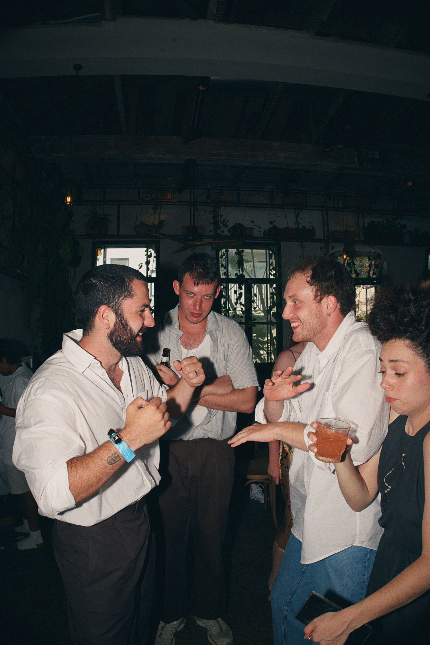 Group of friends socializing at a bar, men in white shirts laughing and gesturing while holding drinks.