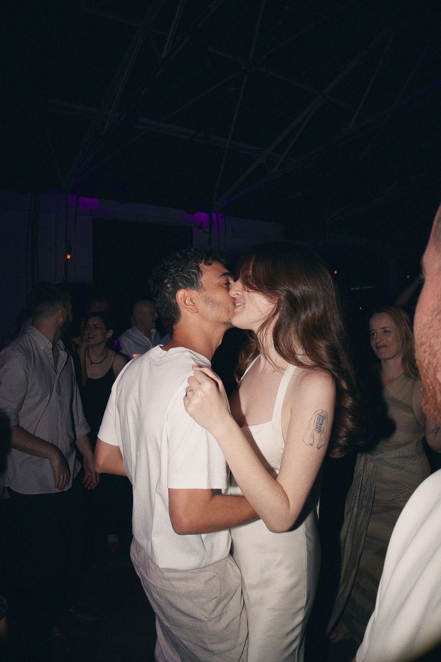 Newlywed couple shares a romantic kiss on the dance floor surrounded by wedding reception guests.