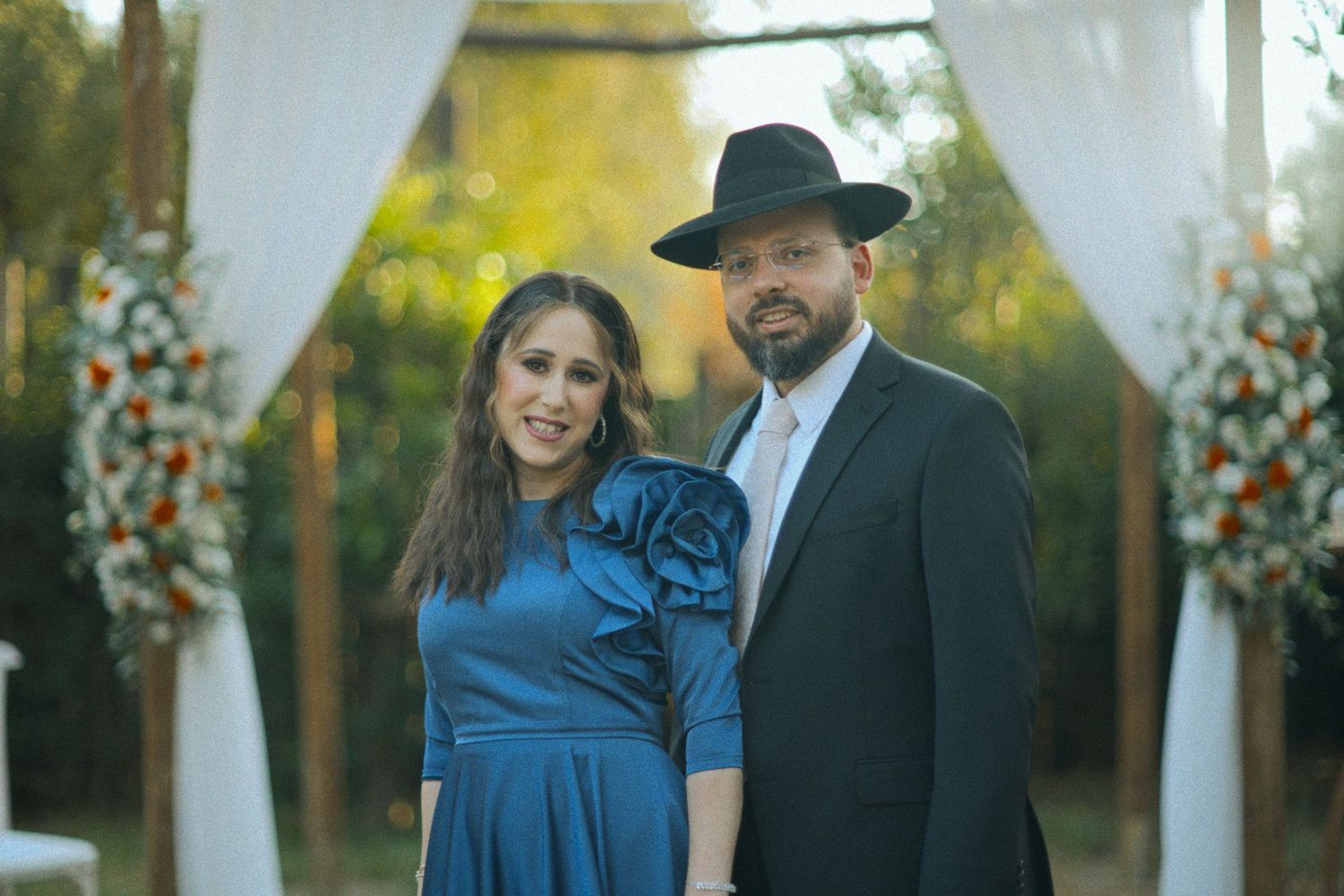 Wedding guests in formal attire interact during outdoor celebration with string lights.