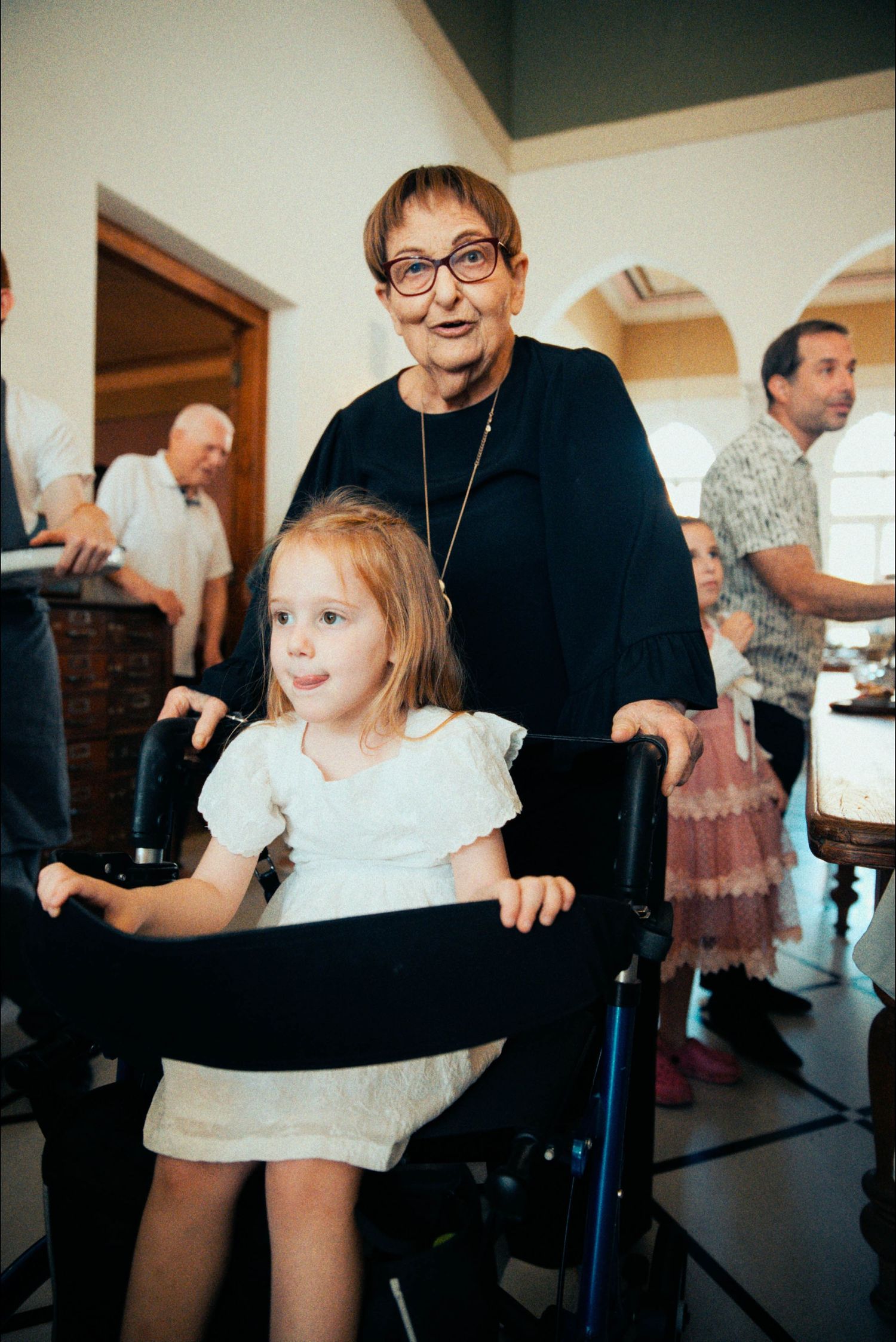 A young child plays with a mobility aid while surrounded by party guests.