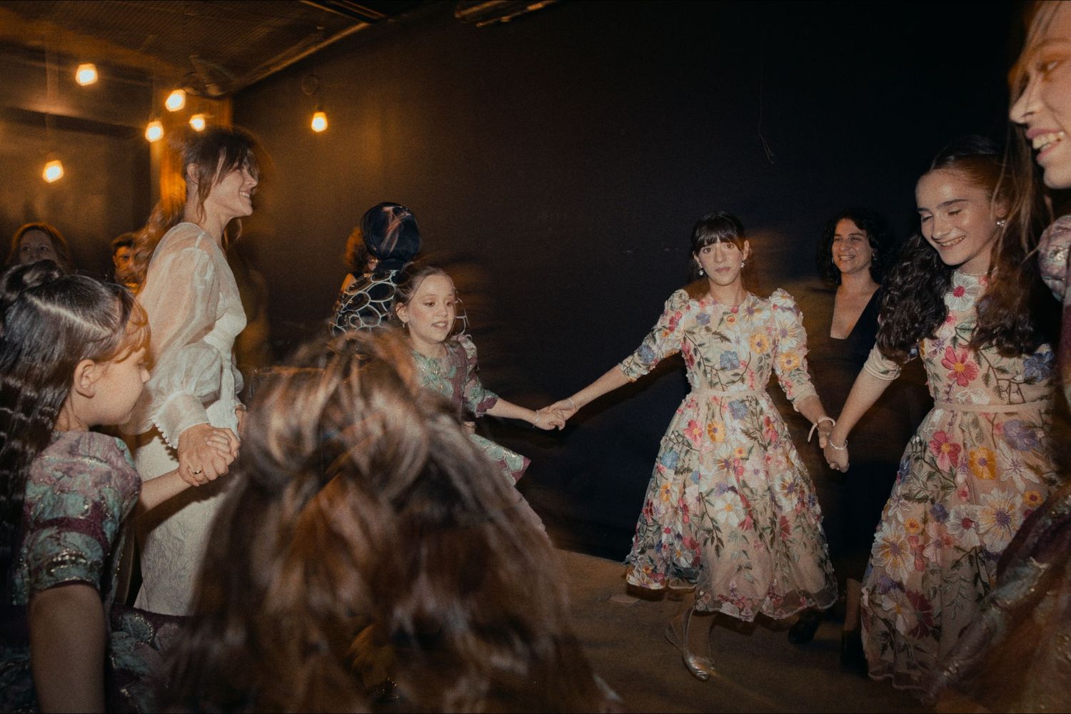 People holding hands in a circle while dancing at a dimly lit indoor party.