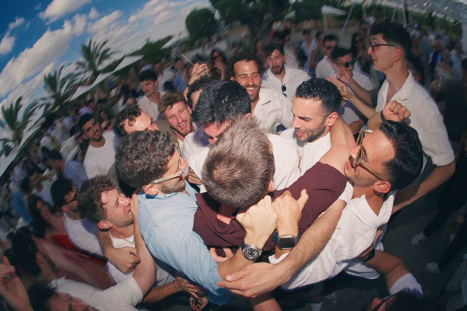 Large group of men in white shirts celebrate together in a joyful outdoor crowd gathering.