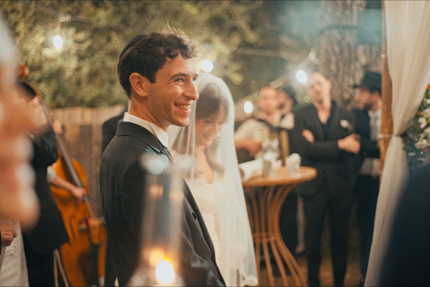 Candlelit outdoor wedding celebration under string lights and white drapery.