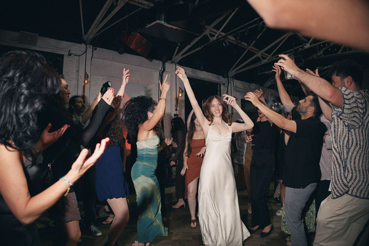 Bride in white dress dancing joyfully with guests at a lively wedding reception party.