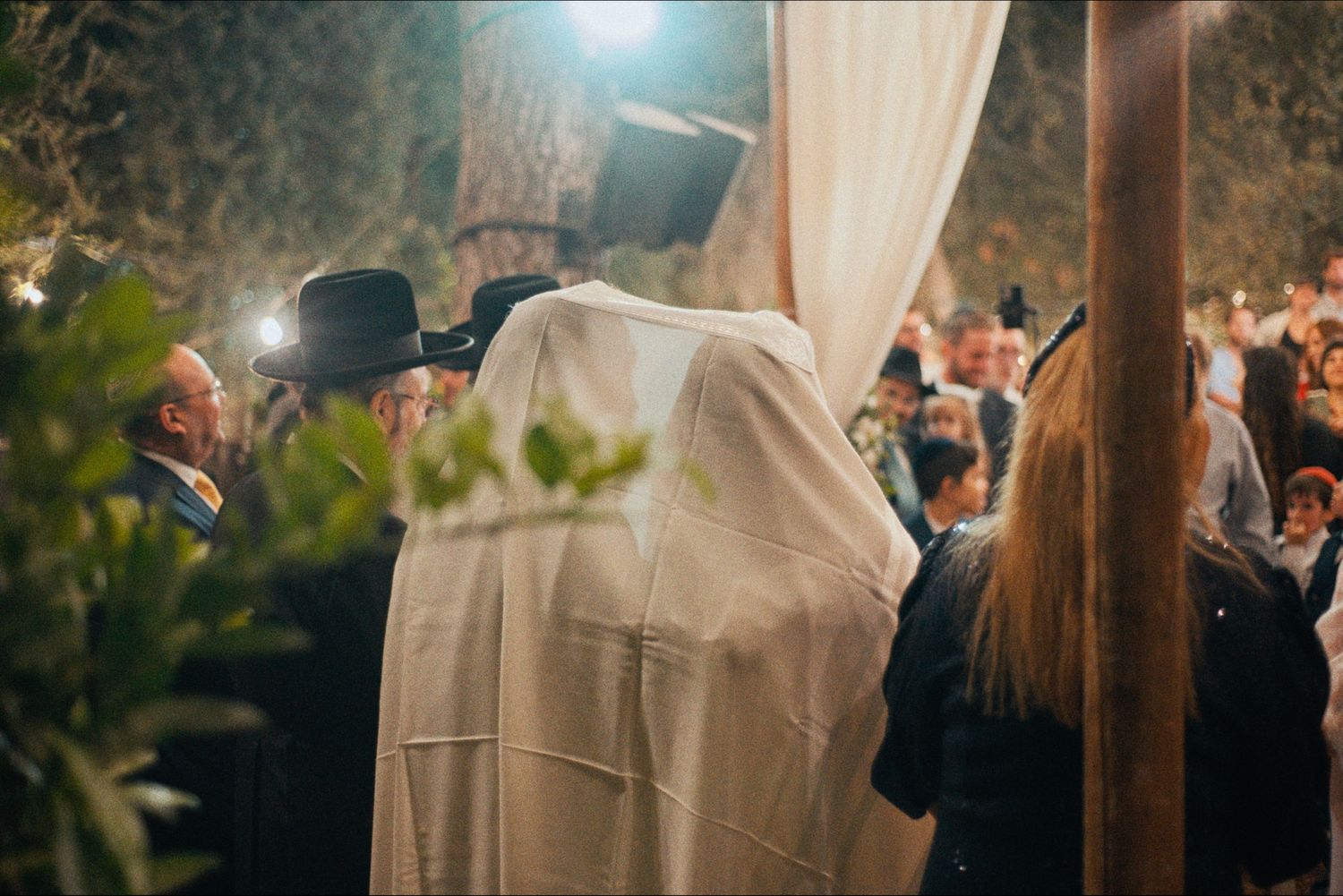 Silhouette of wedding ceremony under moonlit sky with white draping and wooden arch.