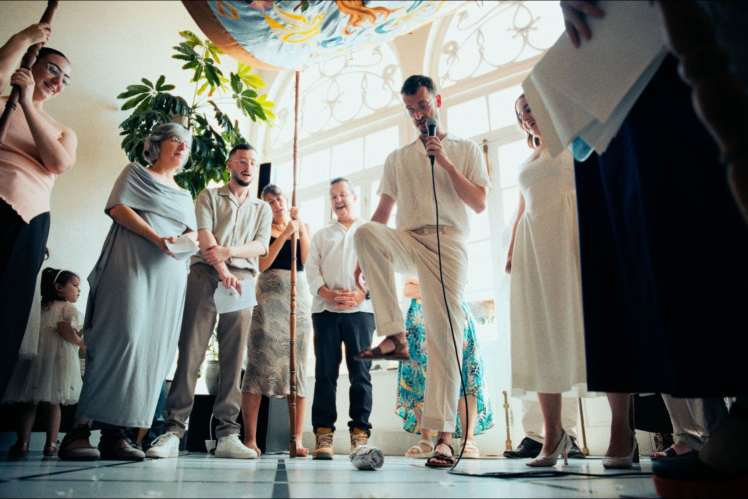 A wedding ceremony takes place in a bright indoor space with decorative ceiling streamers.