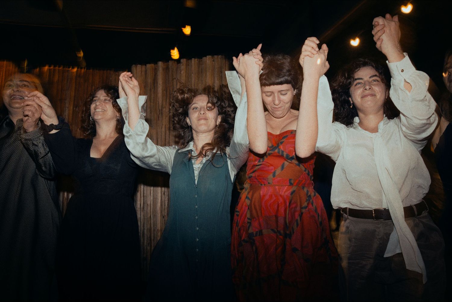 Group of celebrants with raised hands dancing together at a festive indoor gathering.