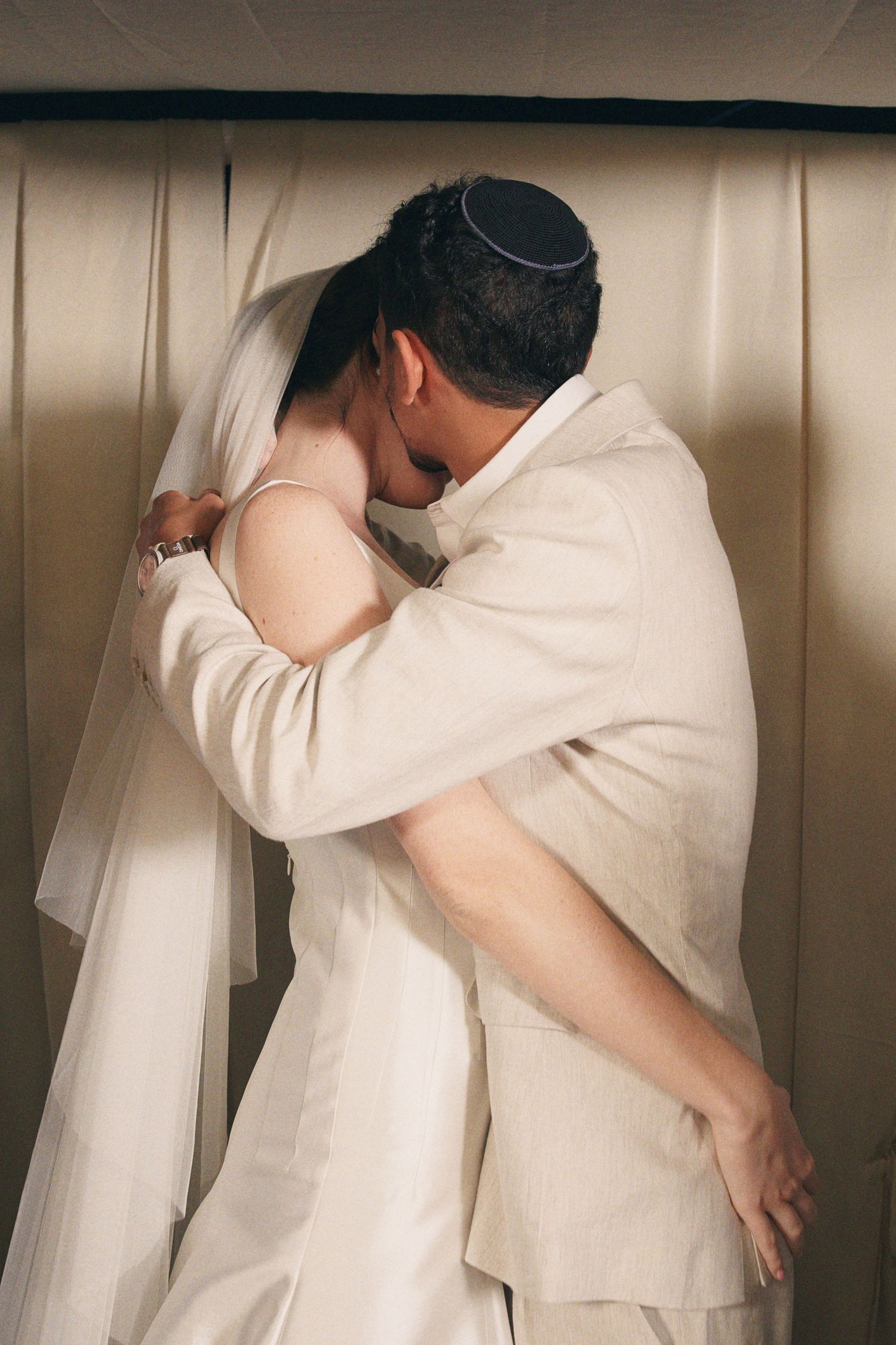 Bride and groom sharing an emotional embrace under a chuppah during Jewish wedding ceremony.