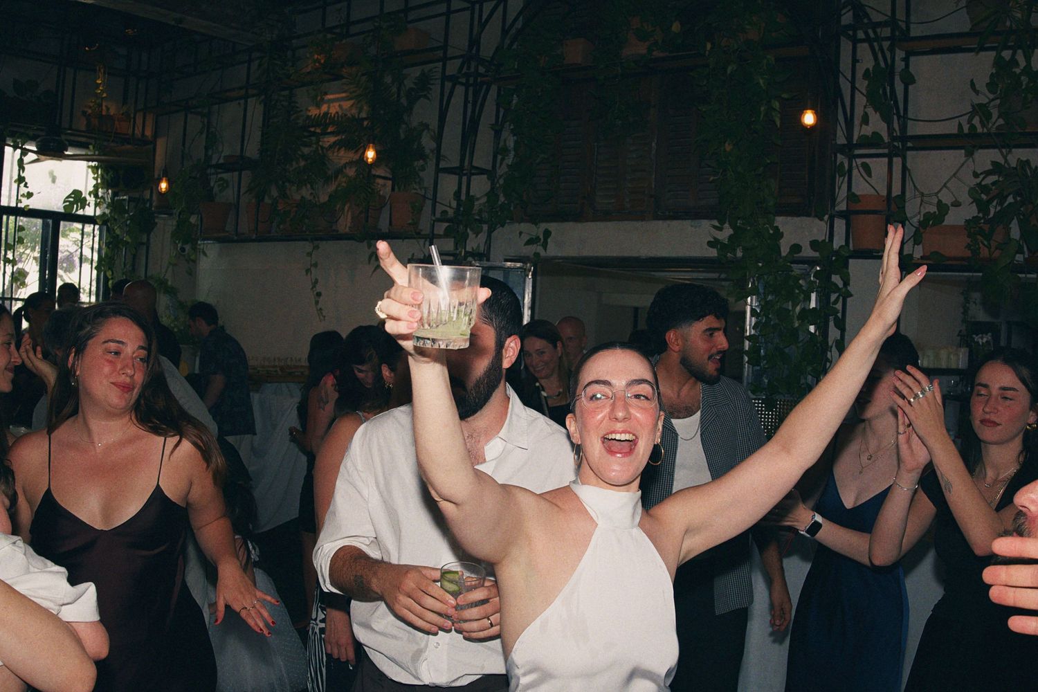 Joyful bride celebrates on dance floor raising glass at lively wedding reception.