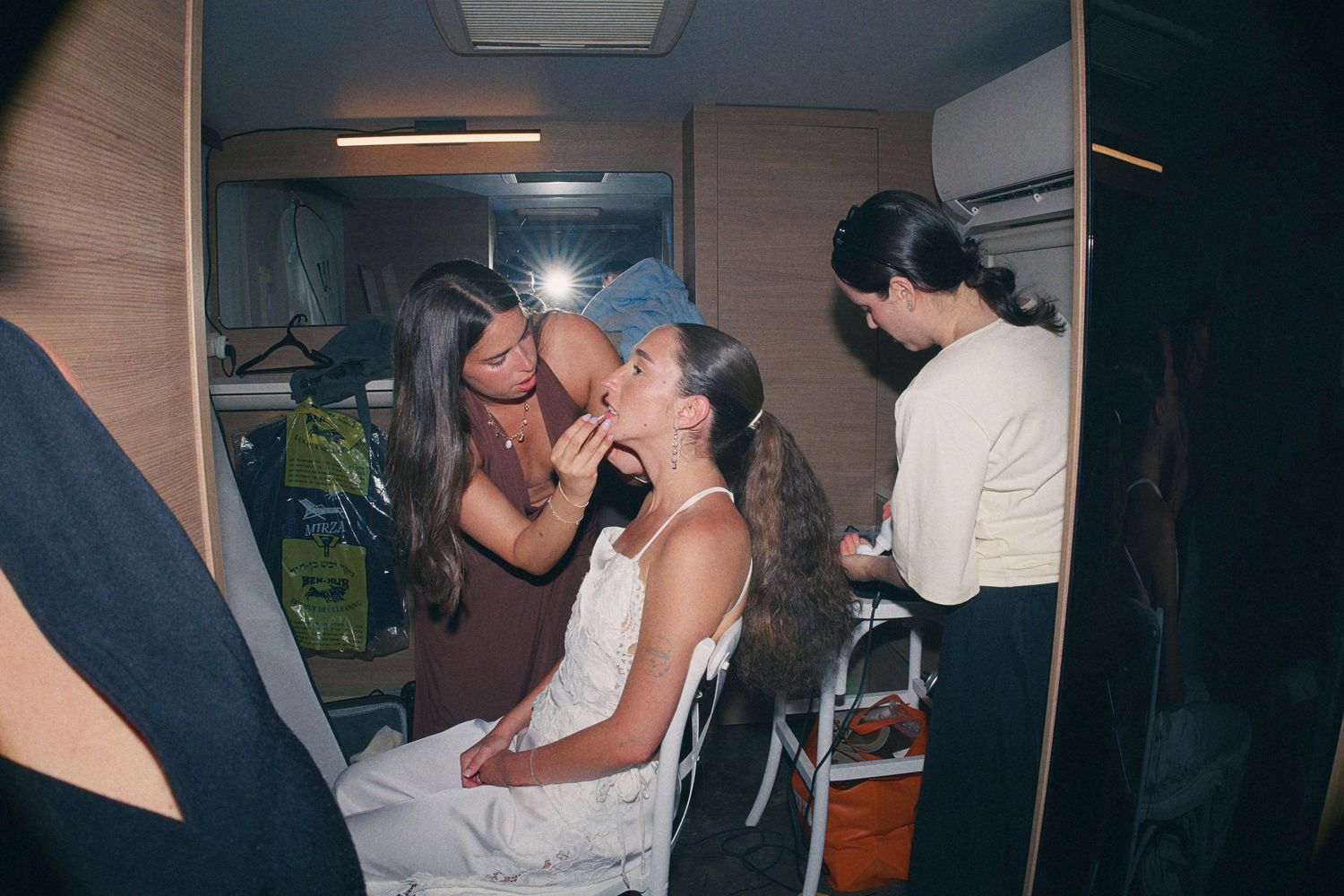 A makeup artist applies makeup to a seated model backstage in a dimly lit dressing room before a fashion show.
