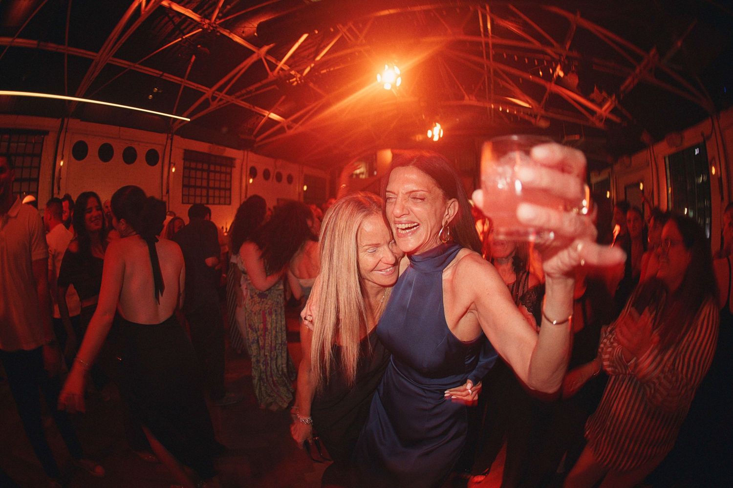 Two women laughing and dancing together at a lively wedding reception party.