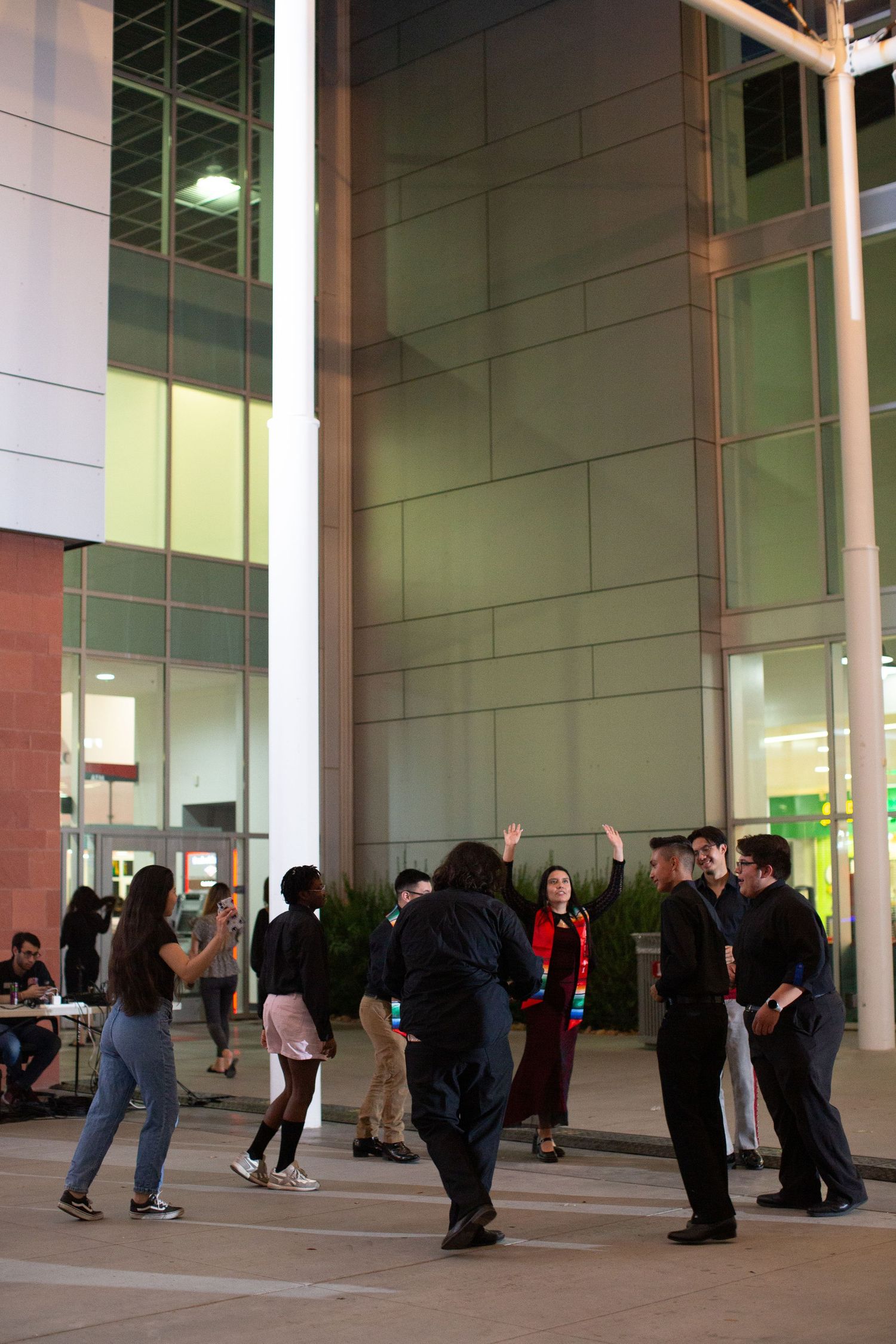 A group of people gathered outside a modern building with large glass windows in the evening.