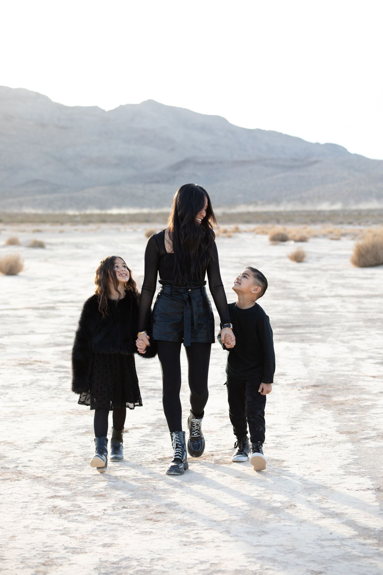 Three people holding hands while walking together on a salt flat with mountains in the distance.