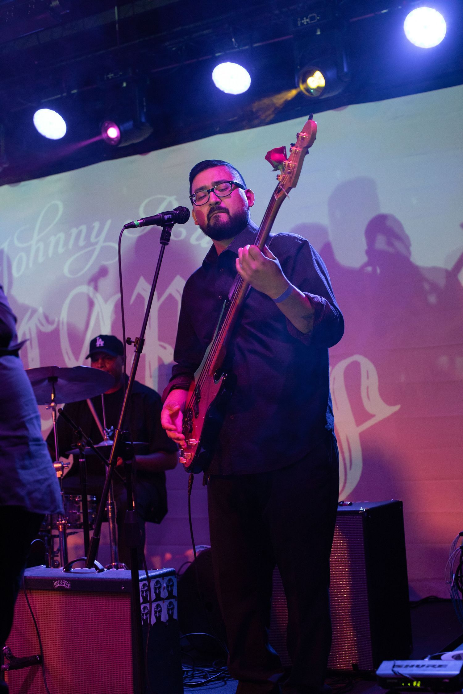 Bass player performs on stage with dramatic pink and blue lighting behind.