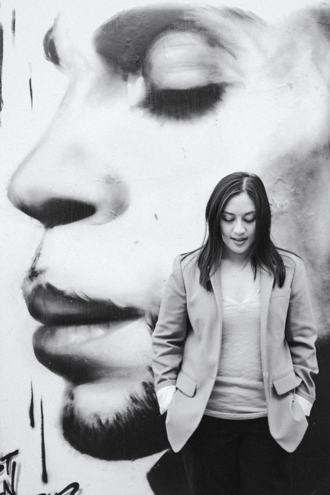 Artistic portrait against large black and white face mural wearing neutral toned outfit.