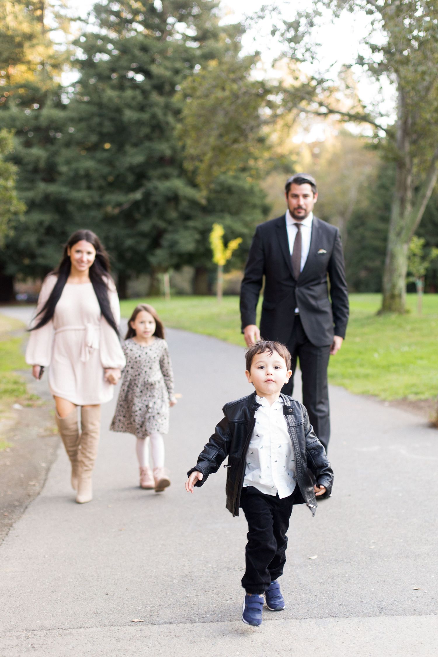 Family walking together on a tree-lined path in formal attire.