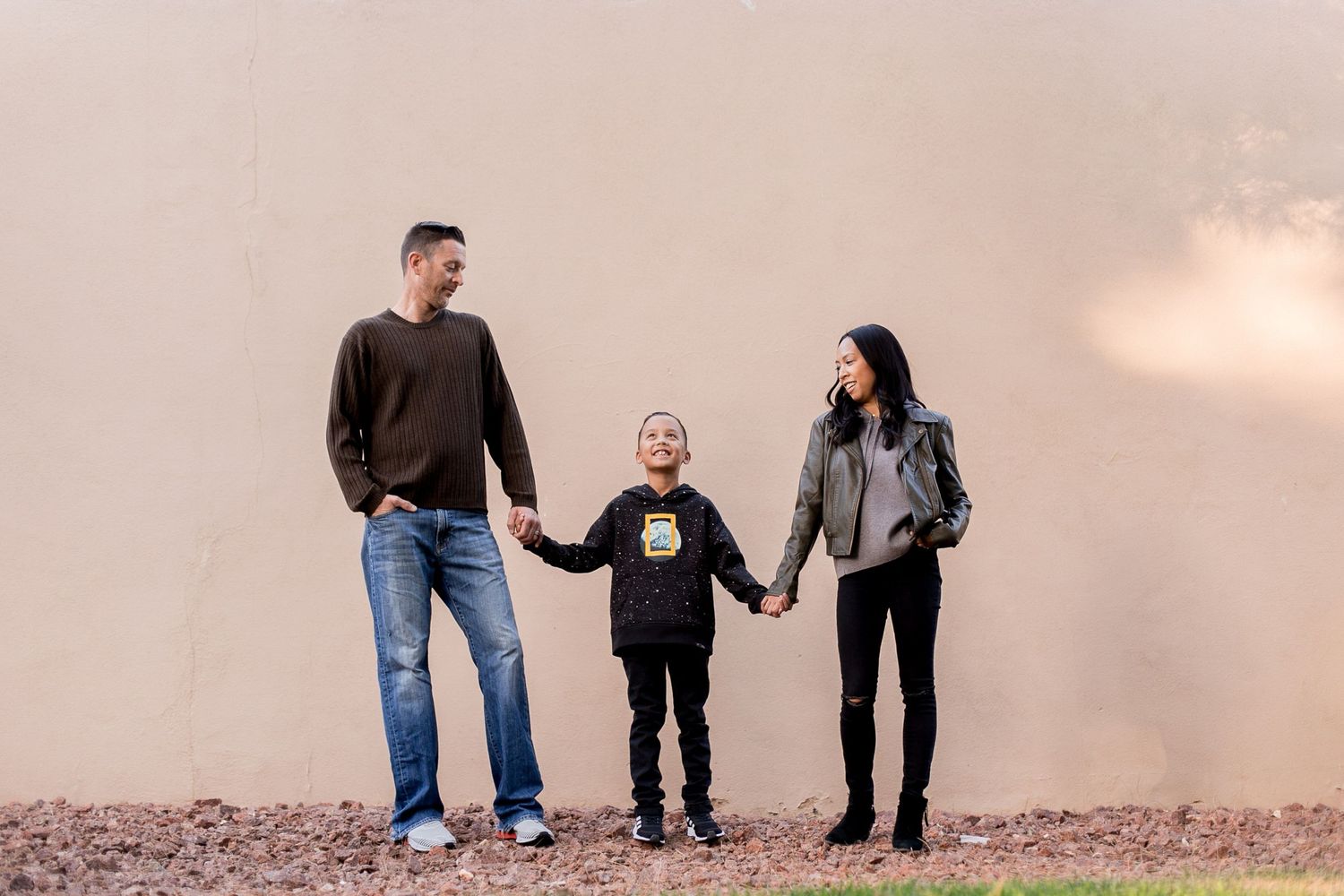 A casual family portrait outdoors with parents and child holding hands.