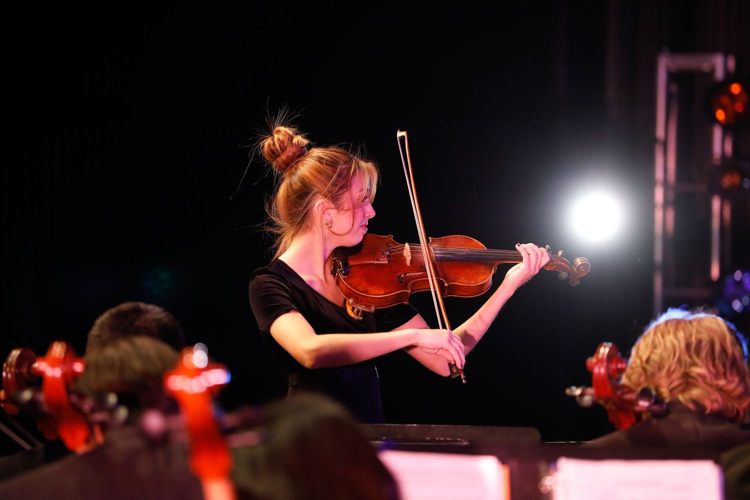 Violinist performing in spotlight during orchestra concert.