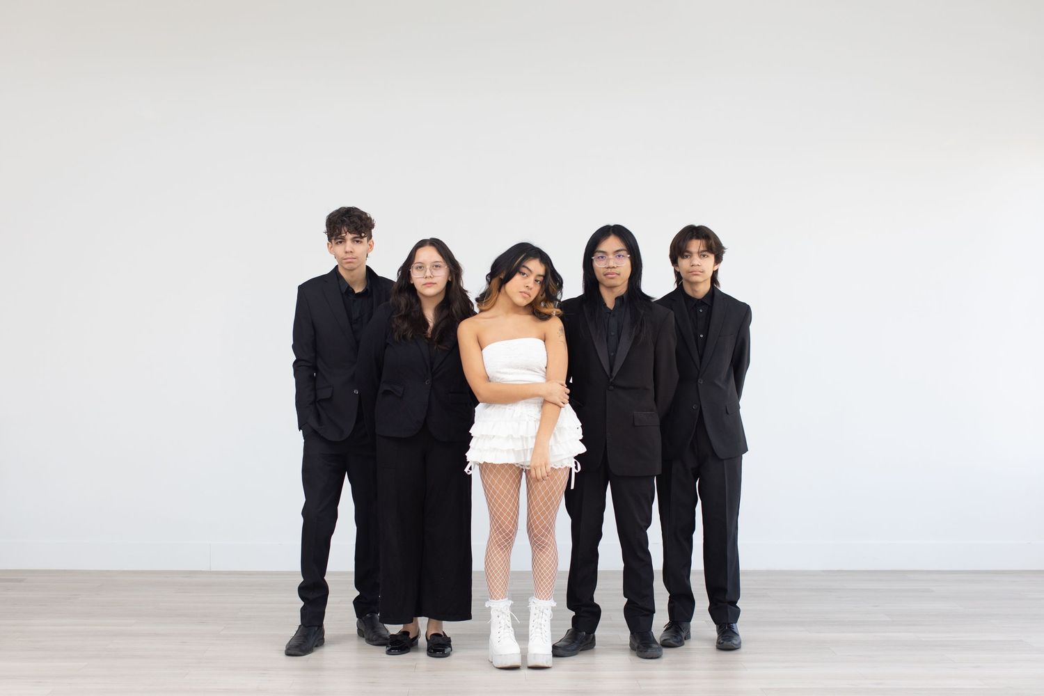 Music group in formal black attire poses with one member in contrasting white outfit.