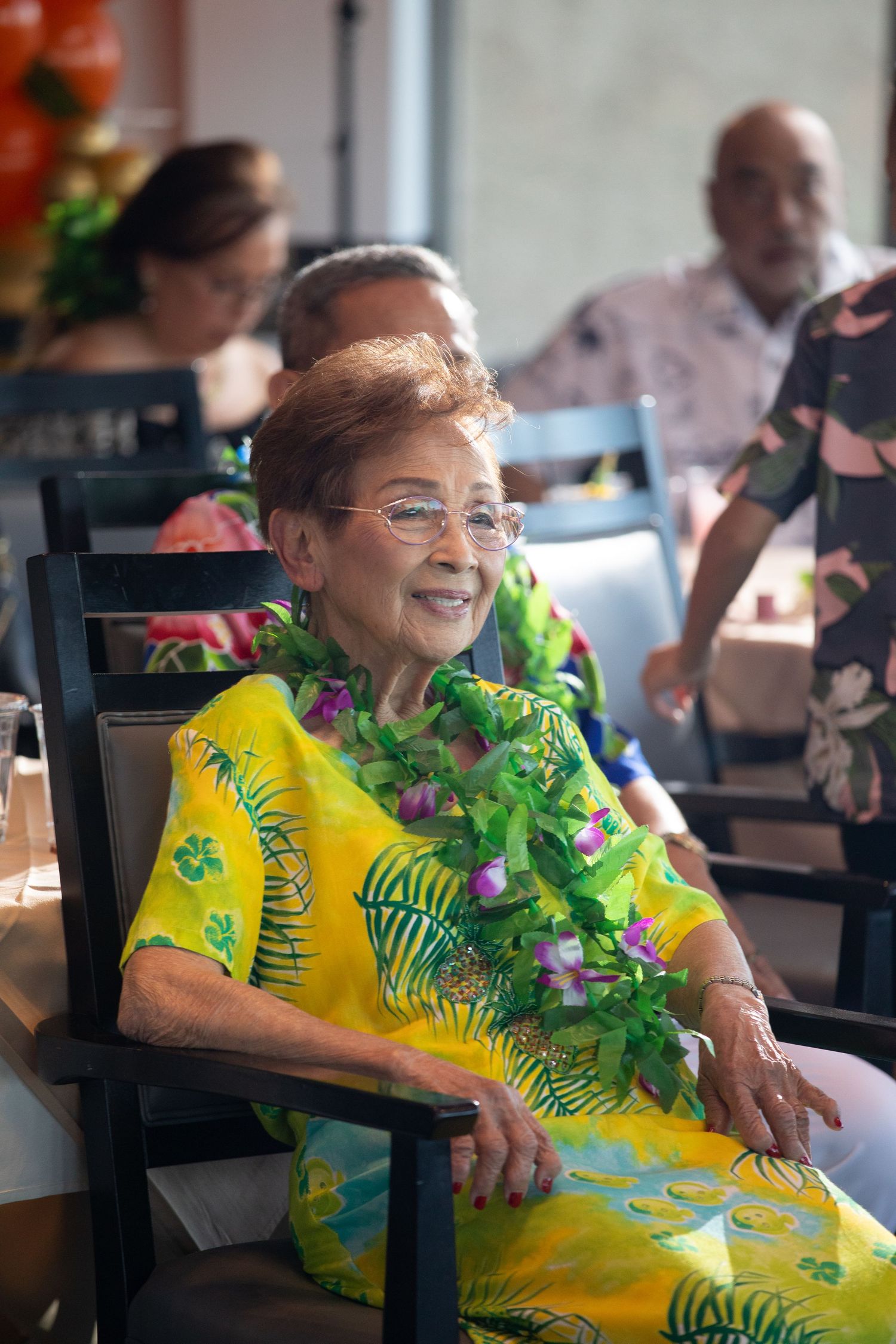 Person wearing bright yellow floral dress with tropical print sitting in chair at party.