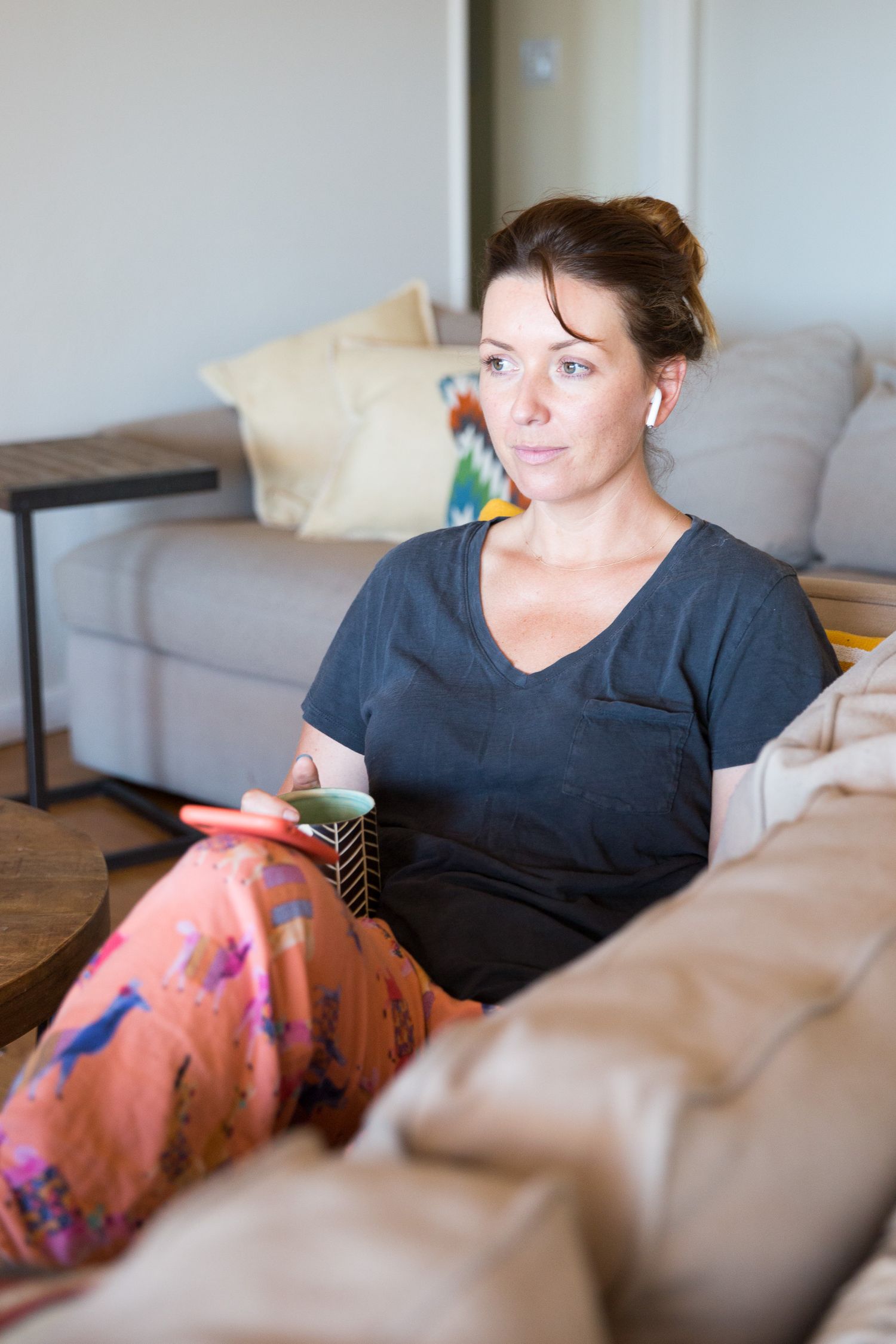 Woman relaxing on gray couch wearing dark shirt and floral pants.