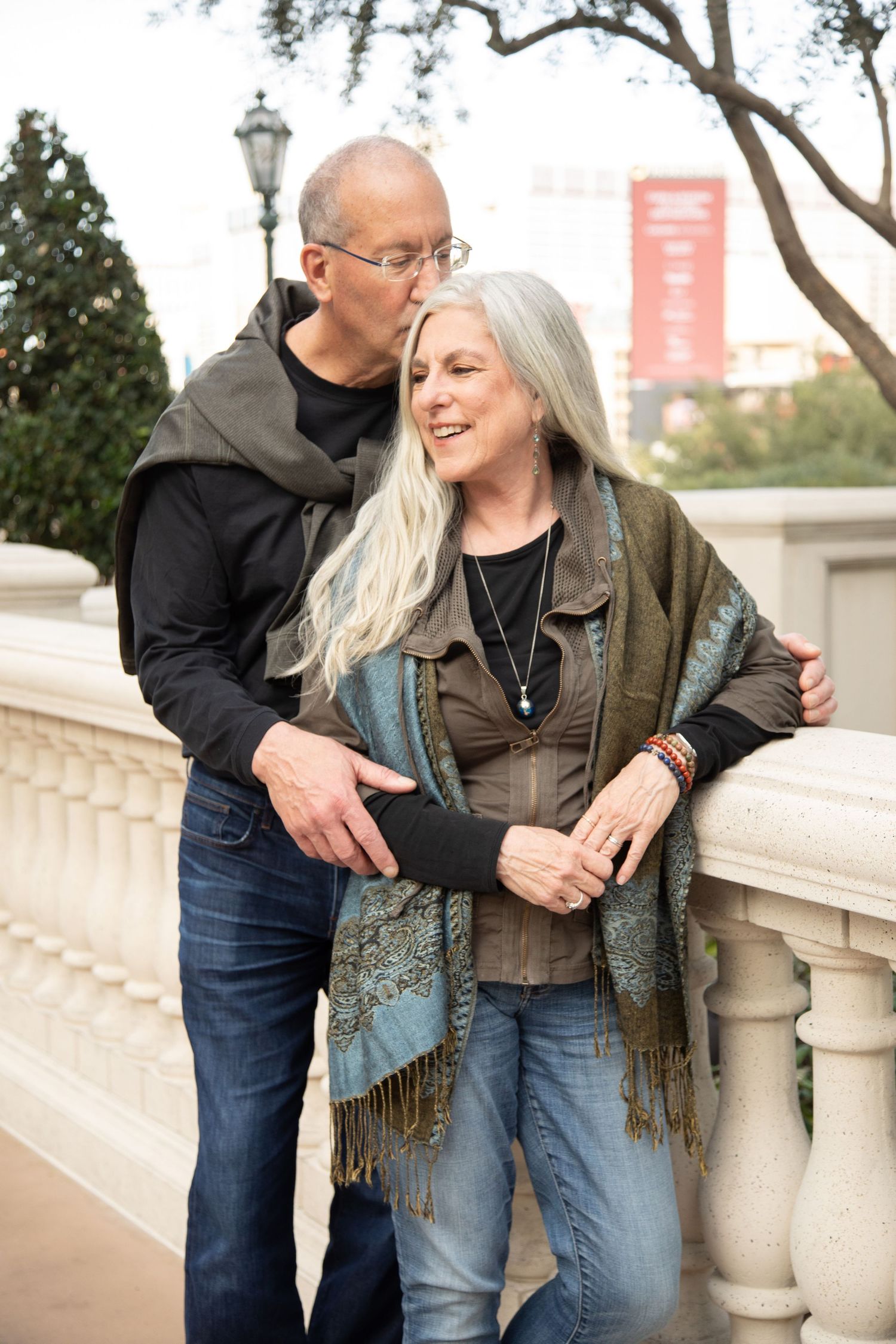 Romantic couple embracing on a stone balcony in casual attire.