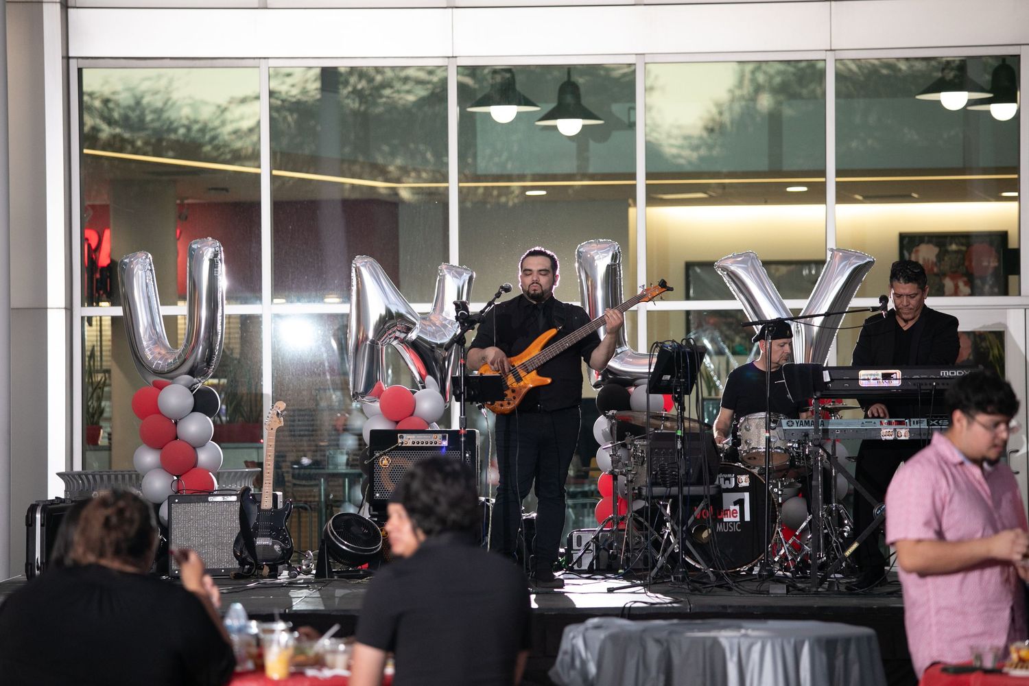 A live band performs on stage with balloons and decorations at an indoor event.
